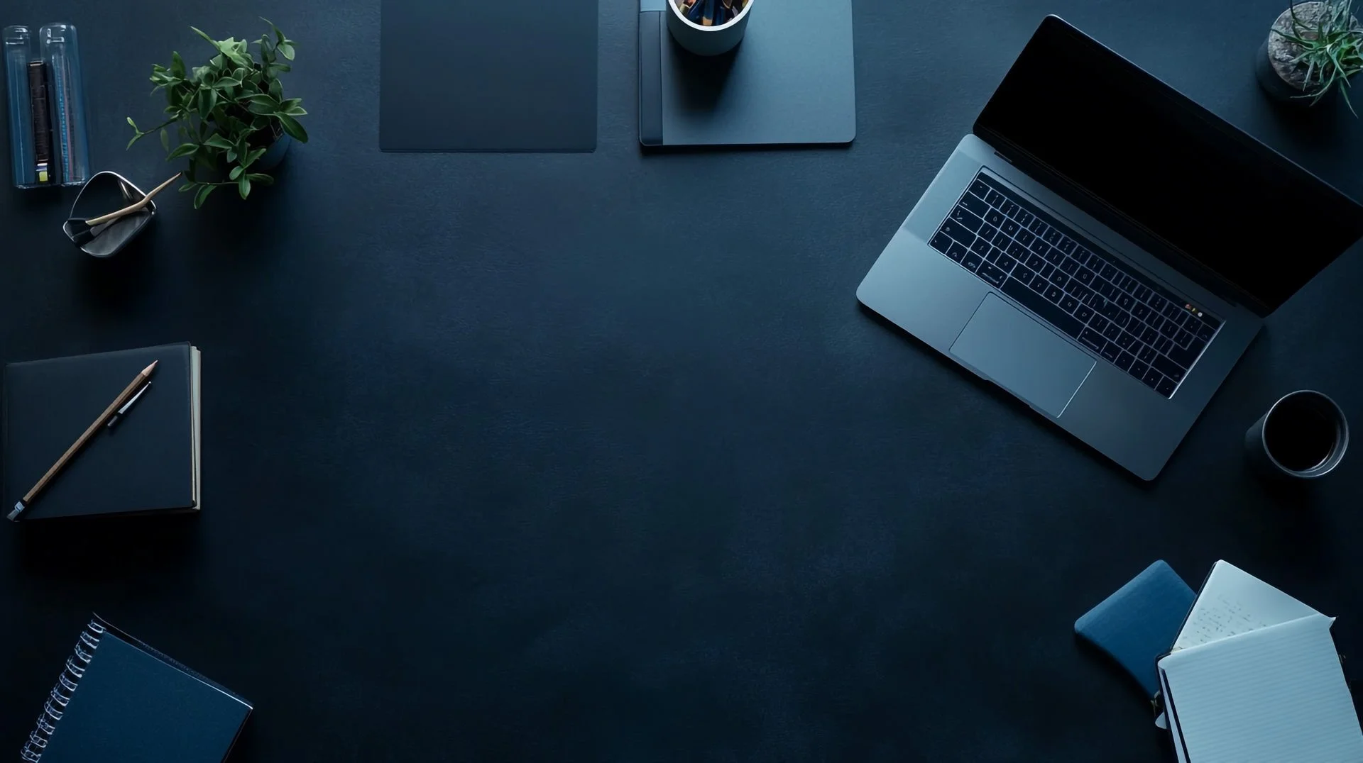 desktop flat lay scene in dark navy with a laptop, coffee and notebooks