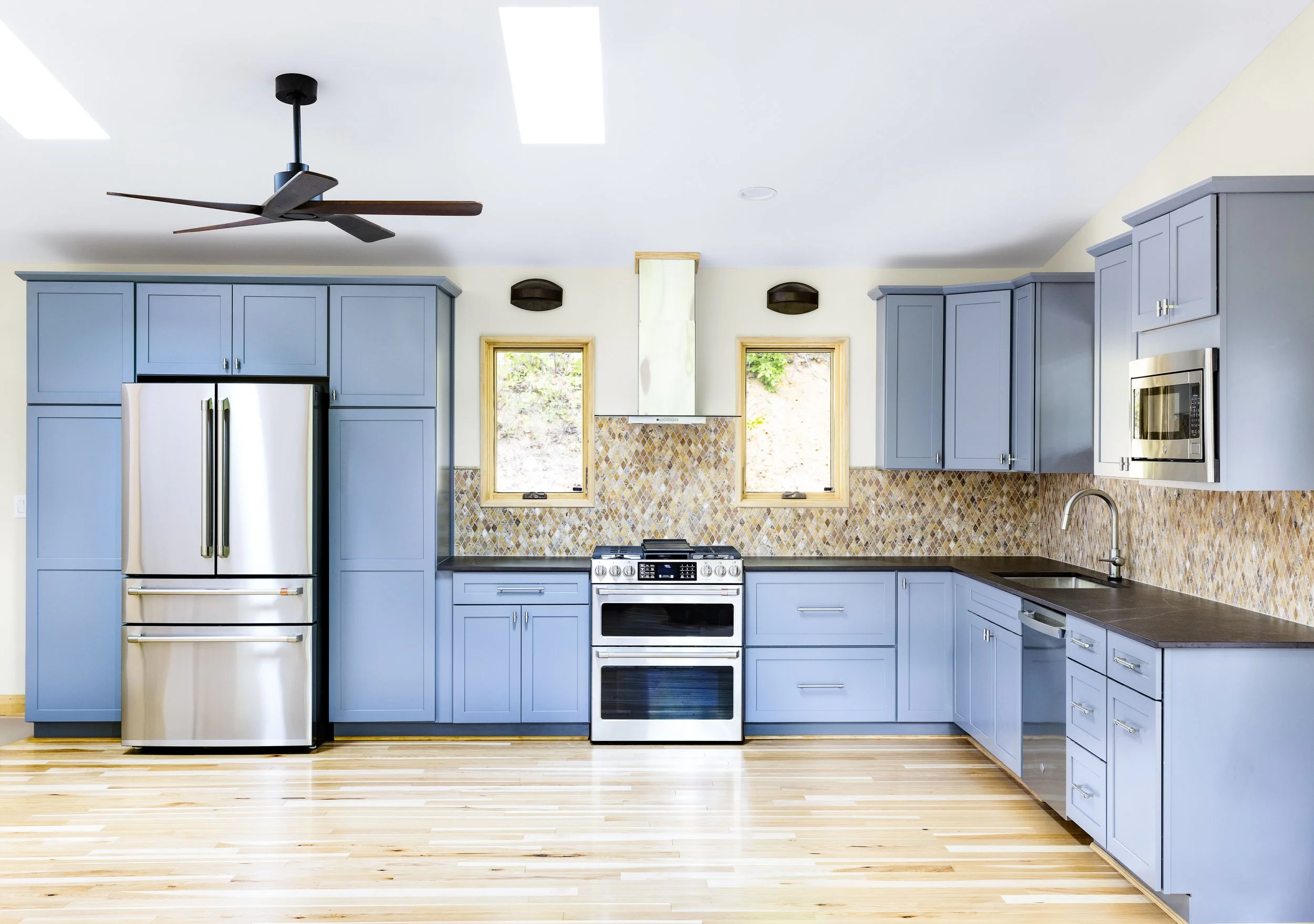 Modern kitchen with blue cabinets, stainless steel appliances, a patterned tile backsplash, and hardwood floors. One of Sunny Day Homes' custom home builds in the High Country of North Carolina.