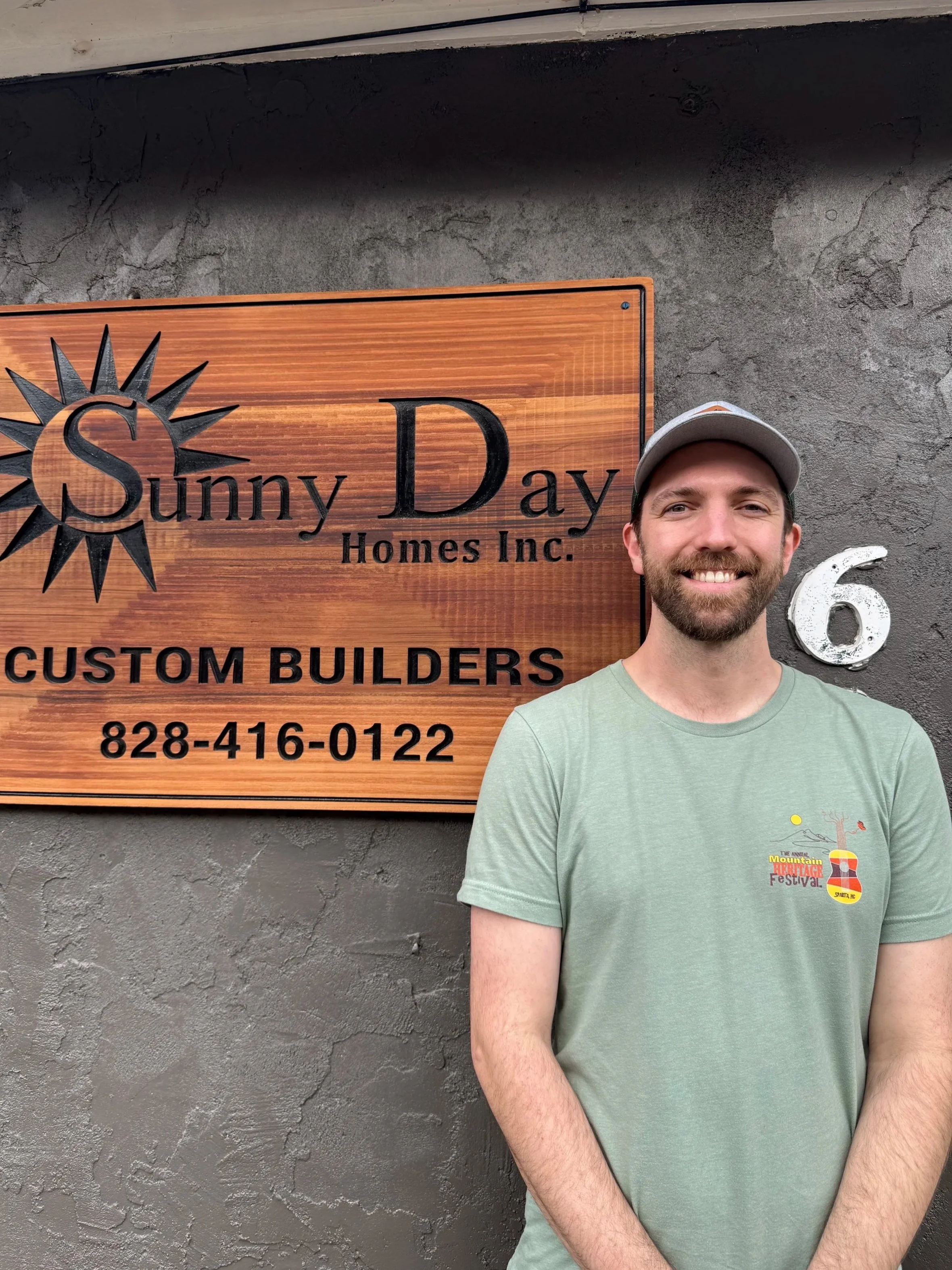 Forest Van Hoose, a man with a beard and short dark hair taking a selfie on a porch with green trees in the background.