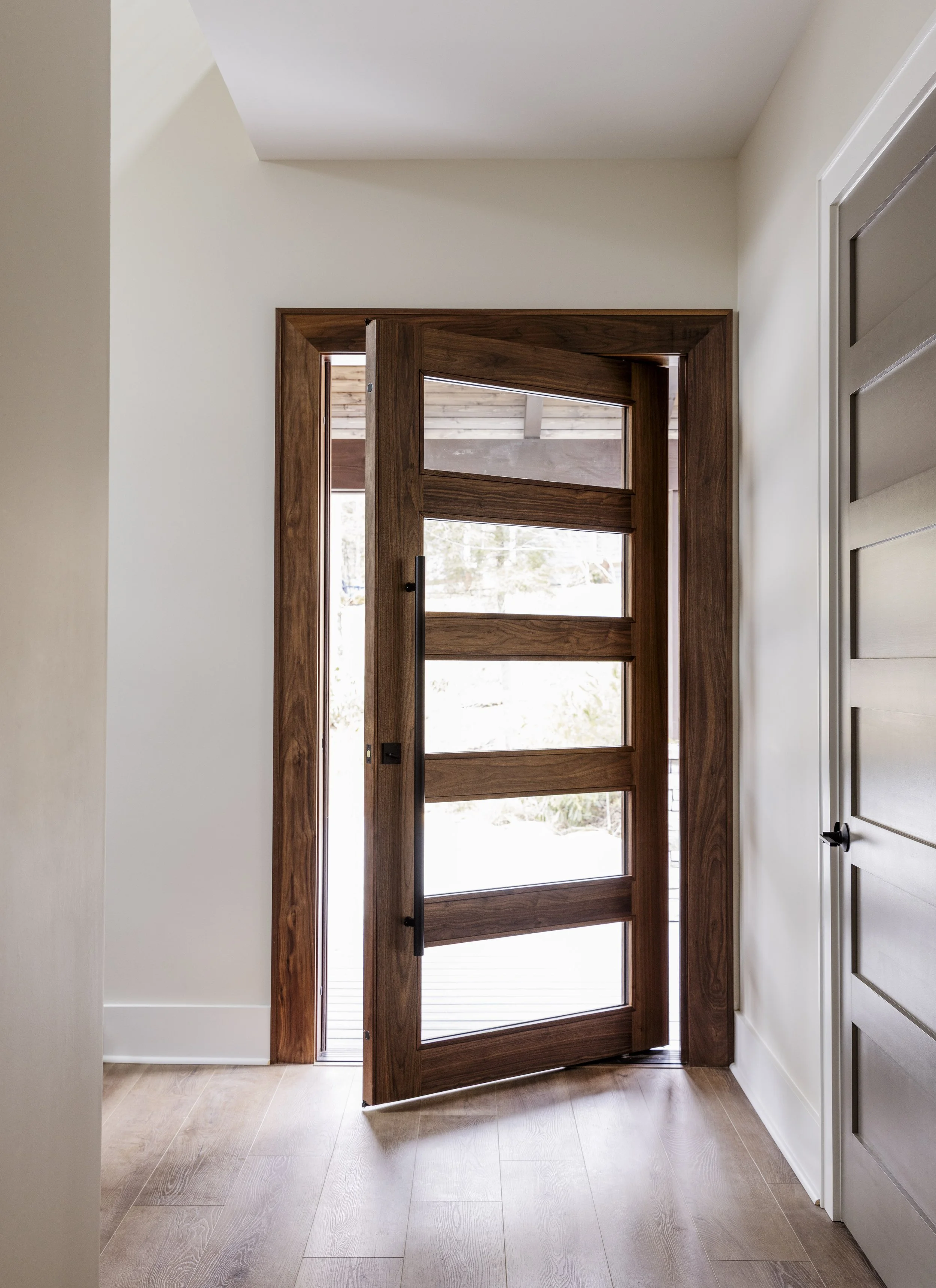 Wooden front door with horizontal glass panels in a modern home interior, open to reveal outside view. One of Sunny Day Homes' custom home builds in Blowing Rock, NC.
