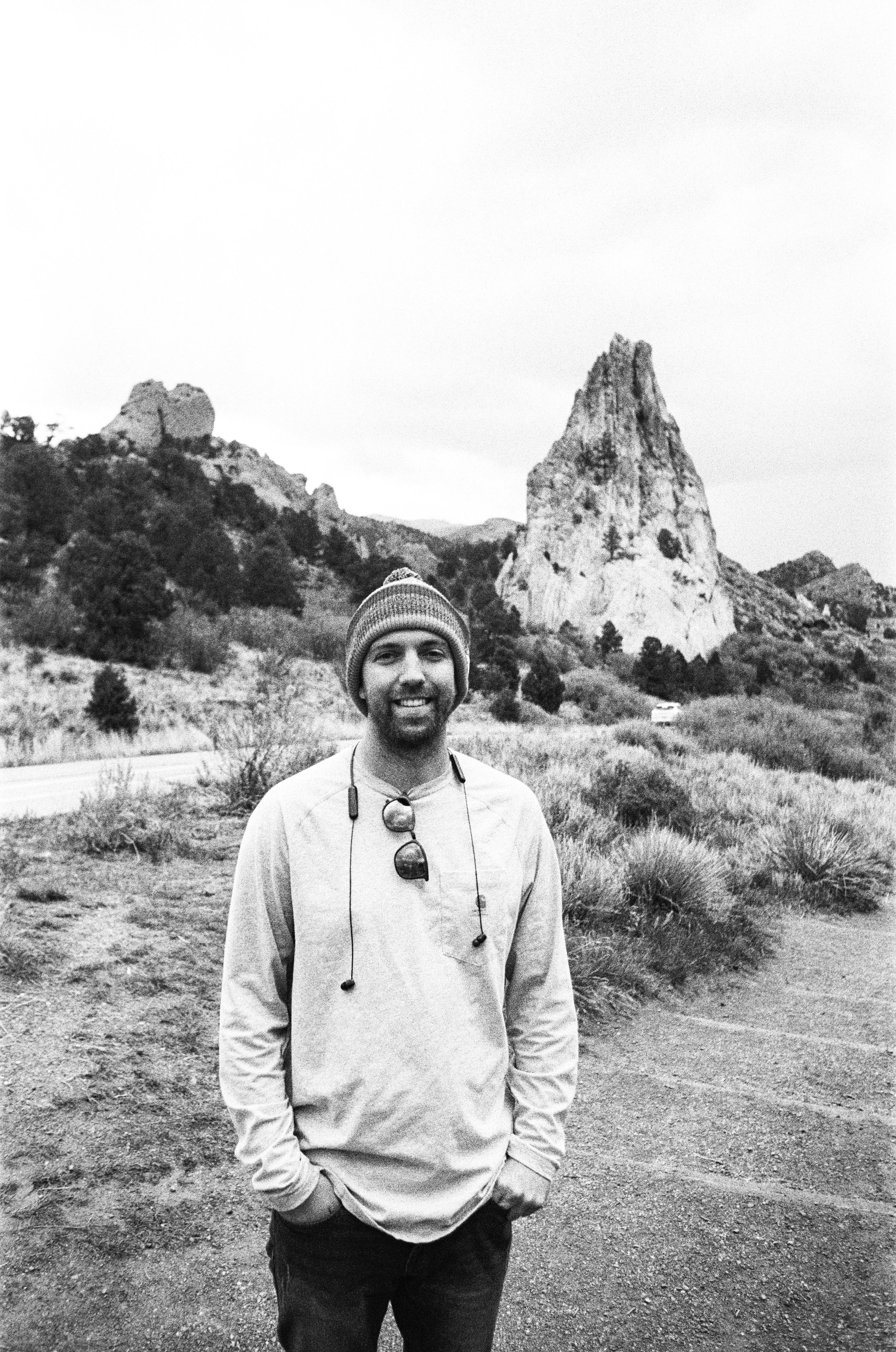Forest Van Hoose, a man with a beard and short dark hair taking a selfie on a porch with green trees in the background.