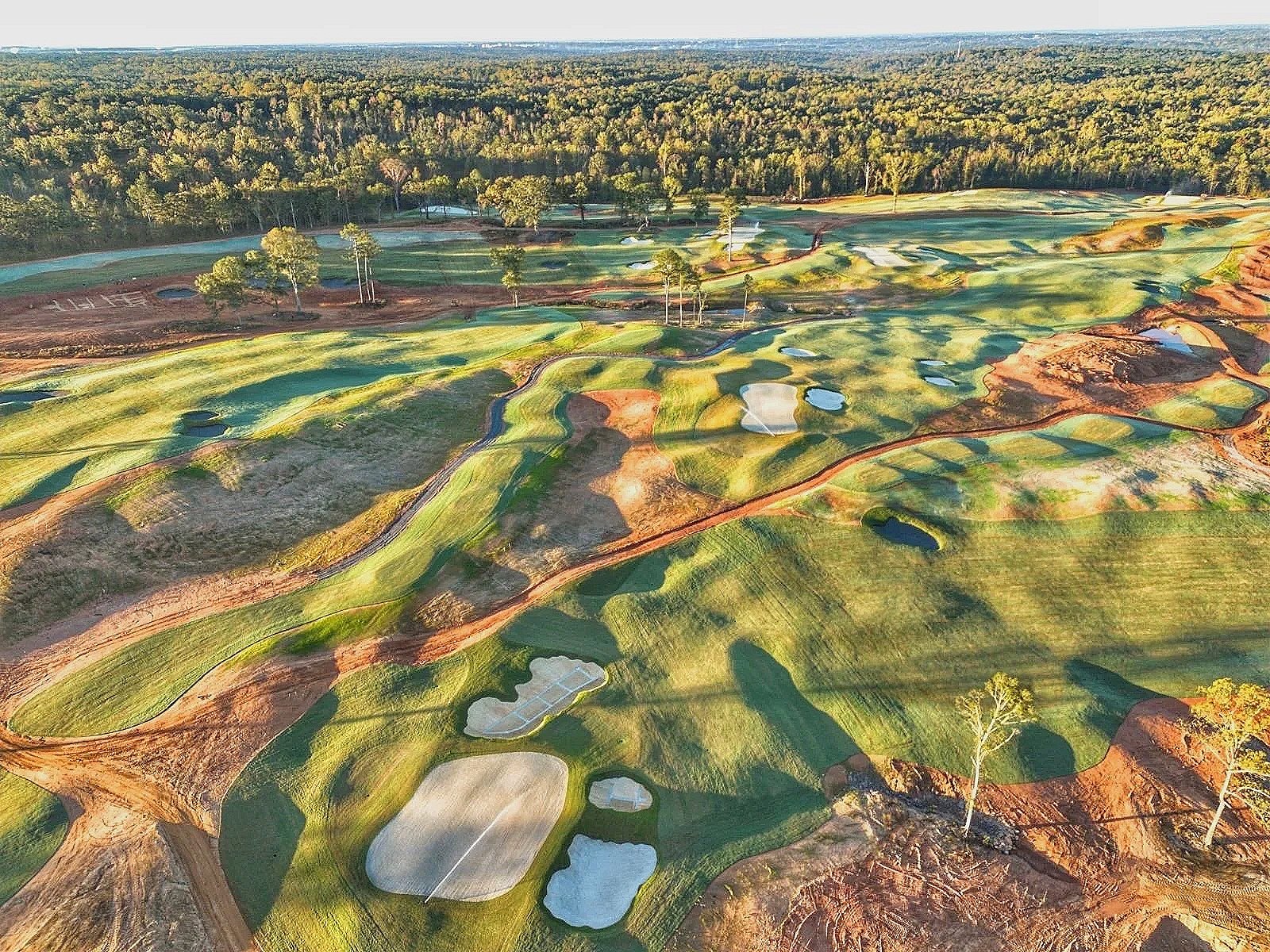 Aerial view of a golf course with multiple greens, sand traps, and fairways amidst trees and natural terrain.