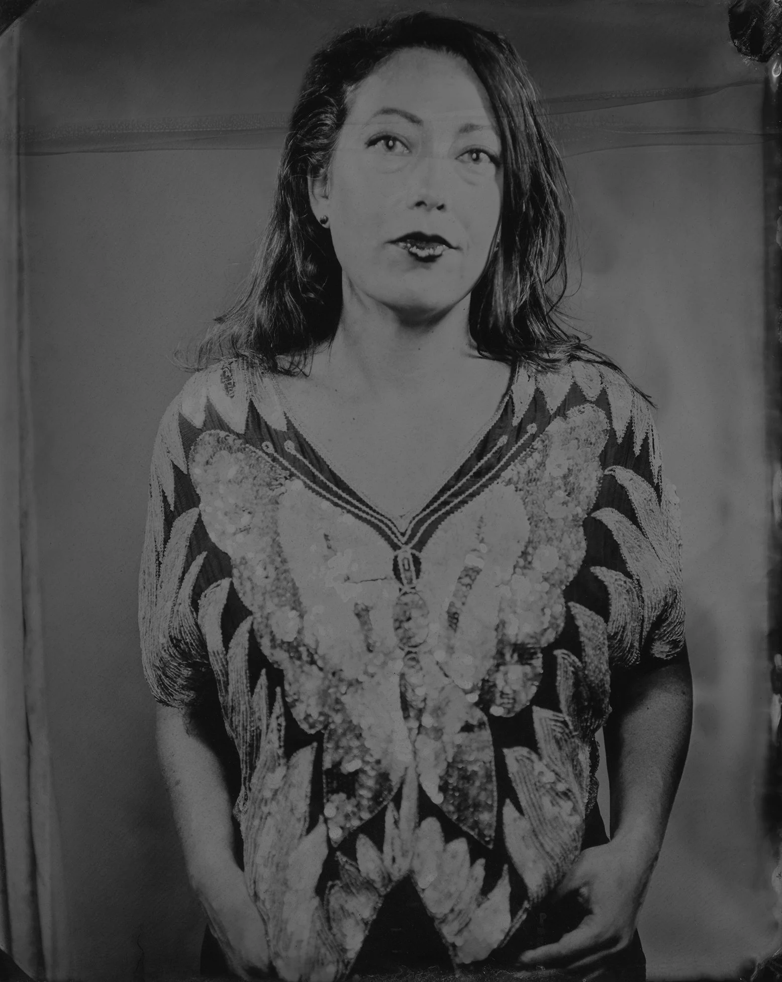 Black and white photograph of a woman with medium-length dark hair, wearing a patterned top with a large butterfly design and hands in her pockets.