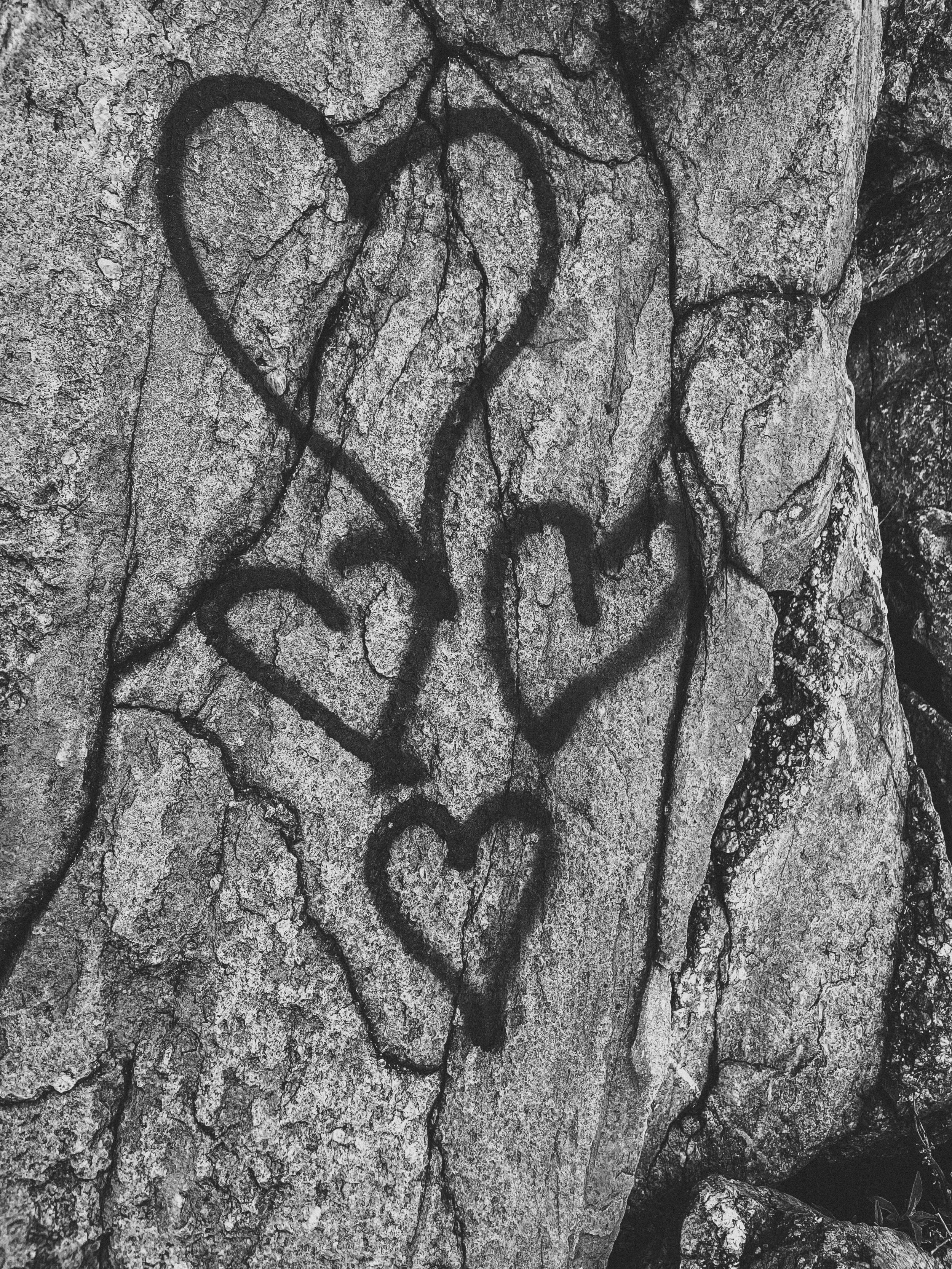 Black graffiti of the word 'LOVE' with two hearts in the middle, painted on a rough, cracked stone surface.