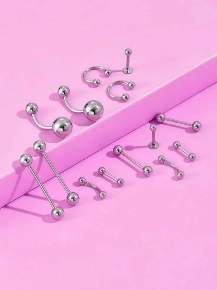 Piercing estetici di vari stili e dimensioni disposti su uno sfondo rosa.