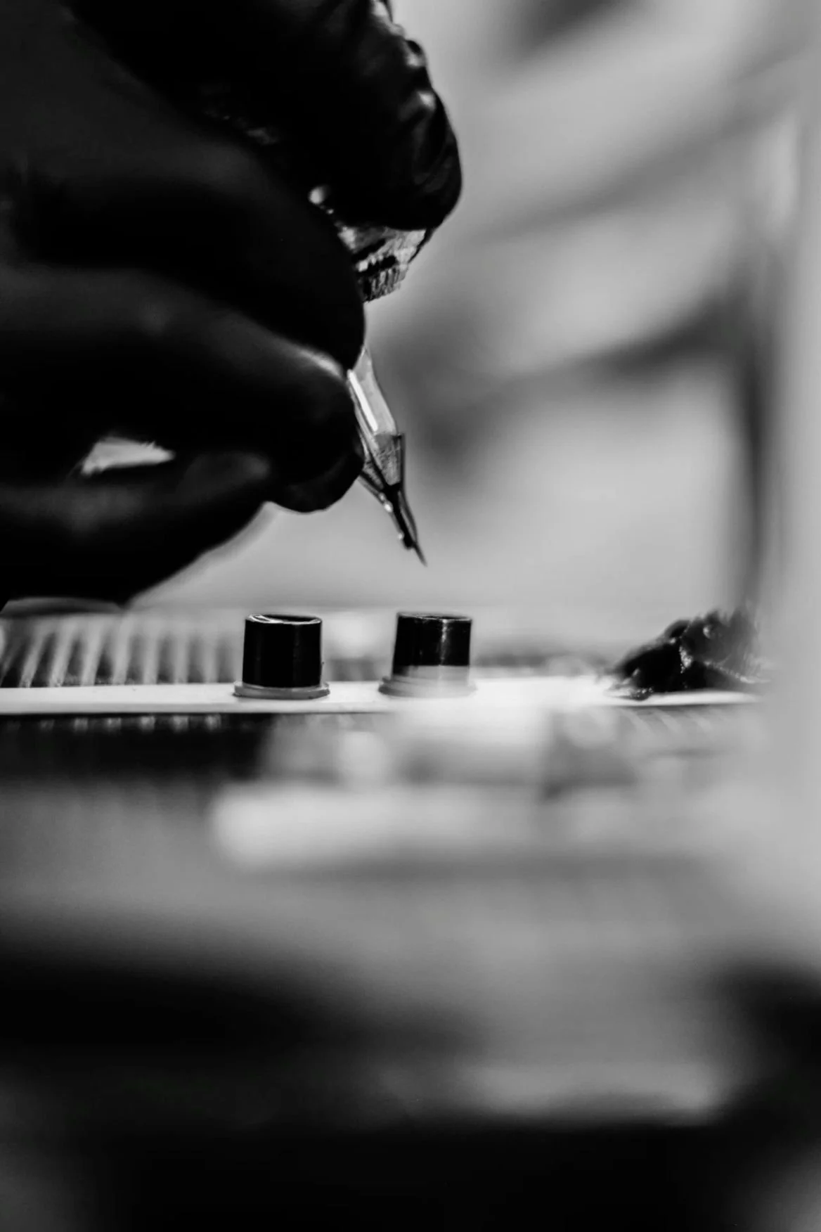 Mano con guanti neri che tiene una penna stilografica e scrive su una tastiera o una superficie piatta, foto in bianco e nero