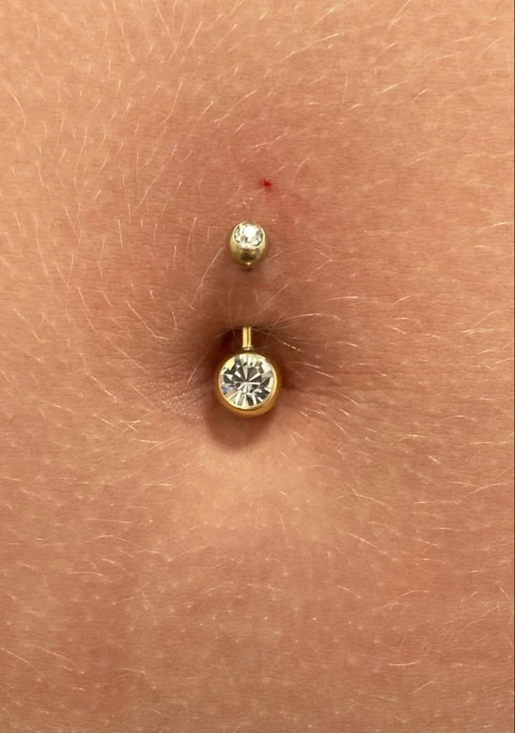 Piercing sull'ombelico con due gioielli, uno con cristallo e uno con pietra più grande, in oro
