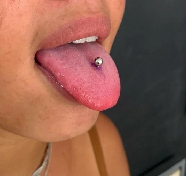 Lingua di una persona con piercings, mostrando una bocca aperta e il tatuaggio sulla lingua