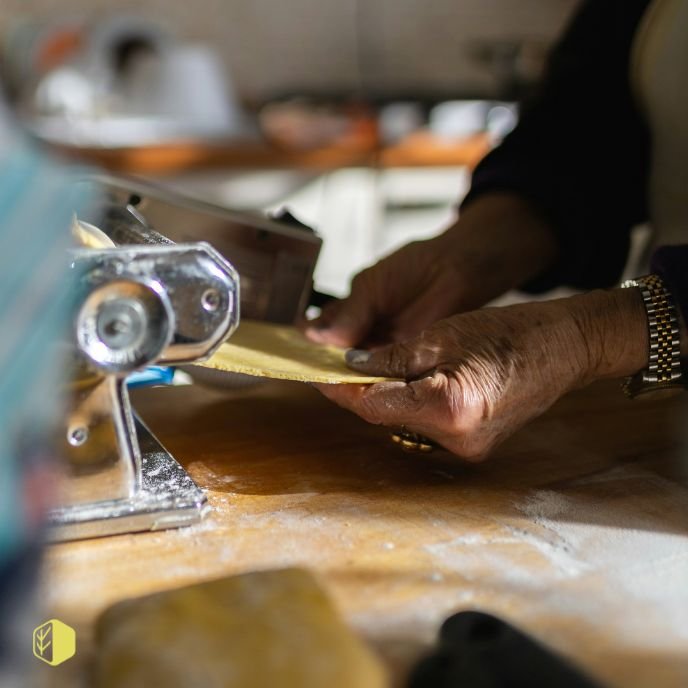 Hands of a person making pasta using a pasta machine on a wooden countertop.