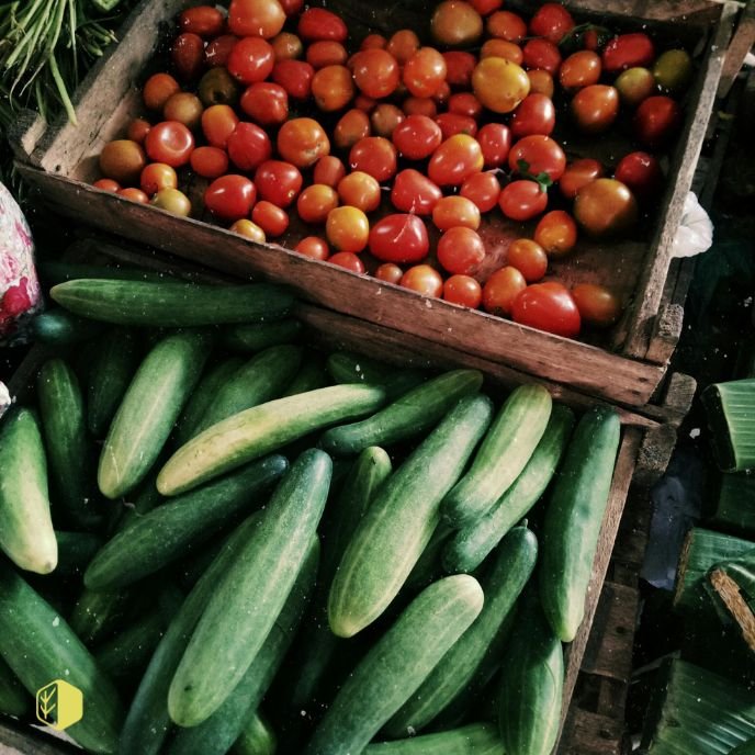 A display of fresh tomatoes in a wooden box and cucumbers in another container.