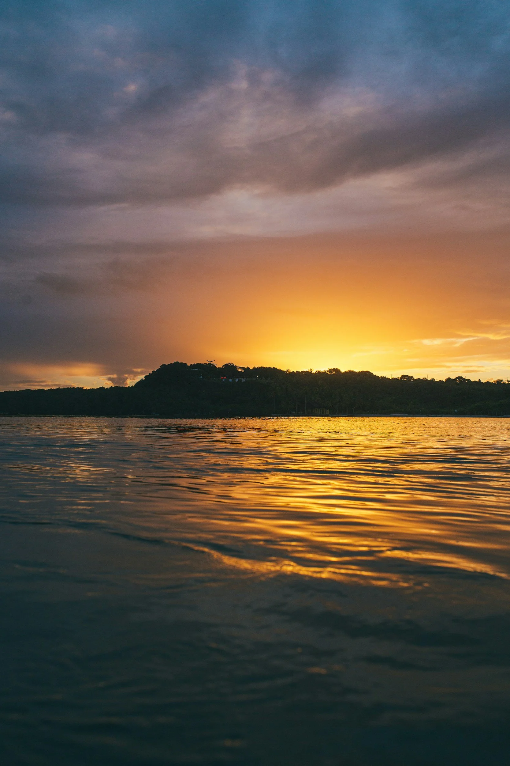 Sunset over a body of water with a silhouette of a hill or island in the distance.