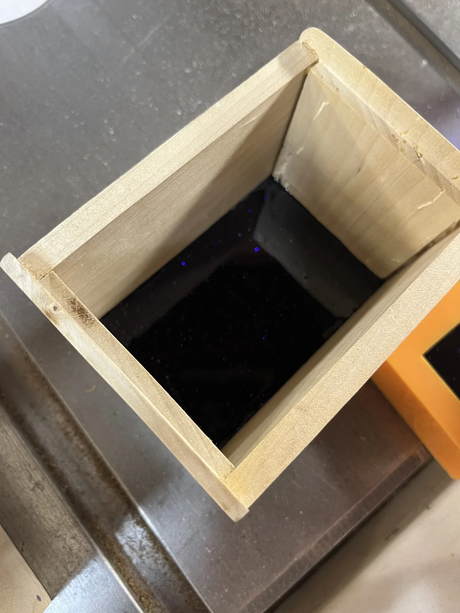 Empty wooden box lined with a black material, sitting on a metallic surface.