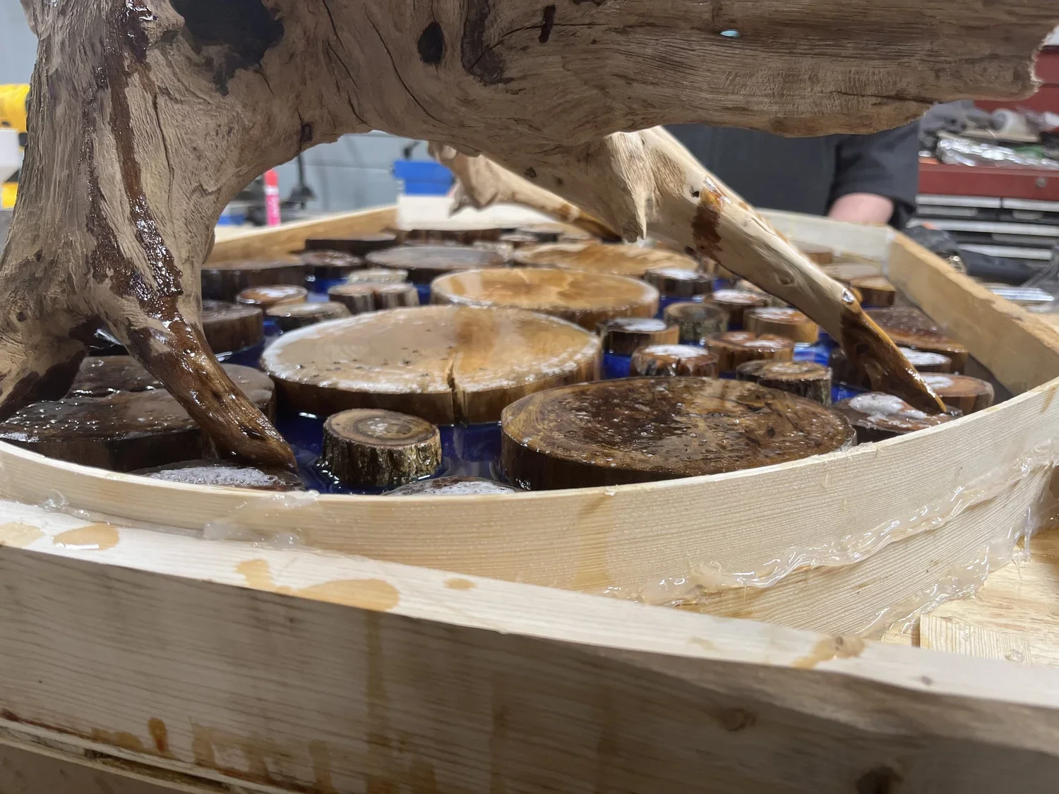 Close-up of a wooden water fountain with polished wooden logs inside, surrounded by water and water splashes, in a workshop setting.
