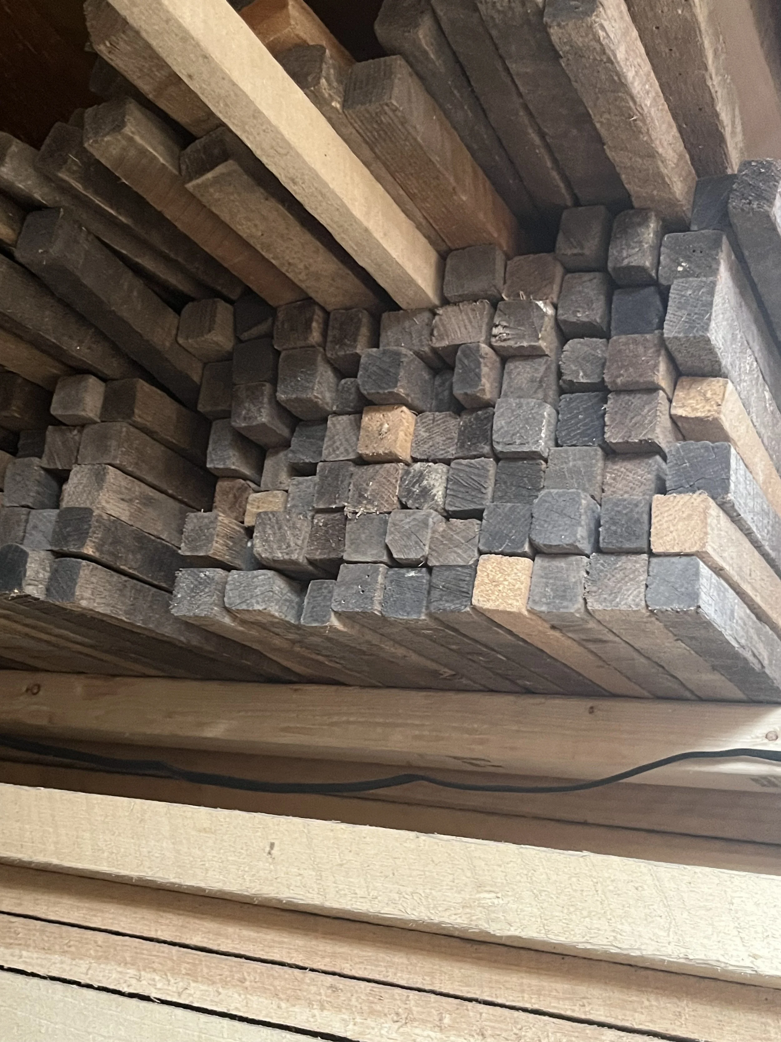 A stack of wooden planks with various sizes, cut into small blocks, stored in a wooden shed or workshop.