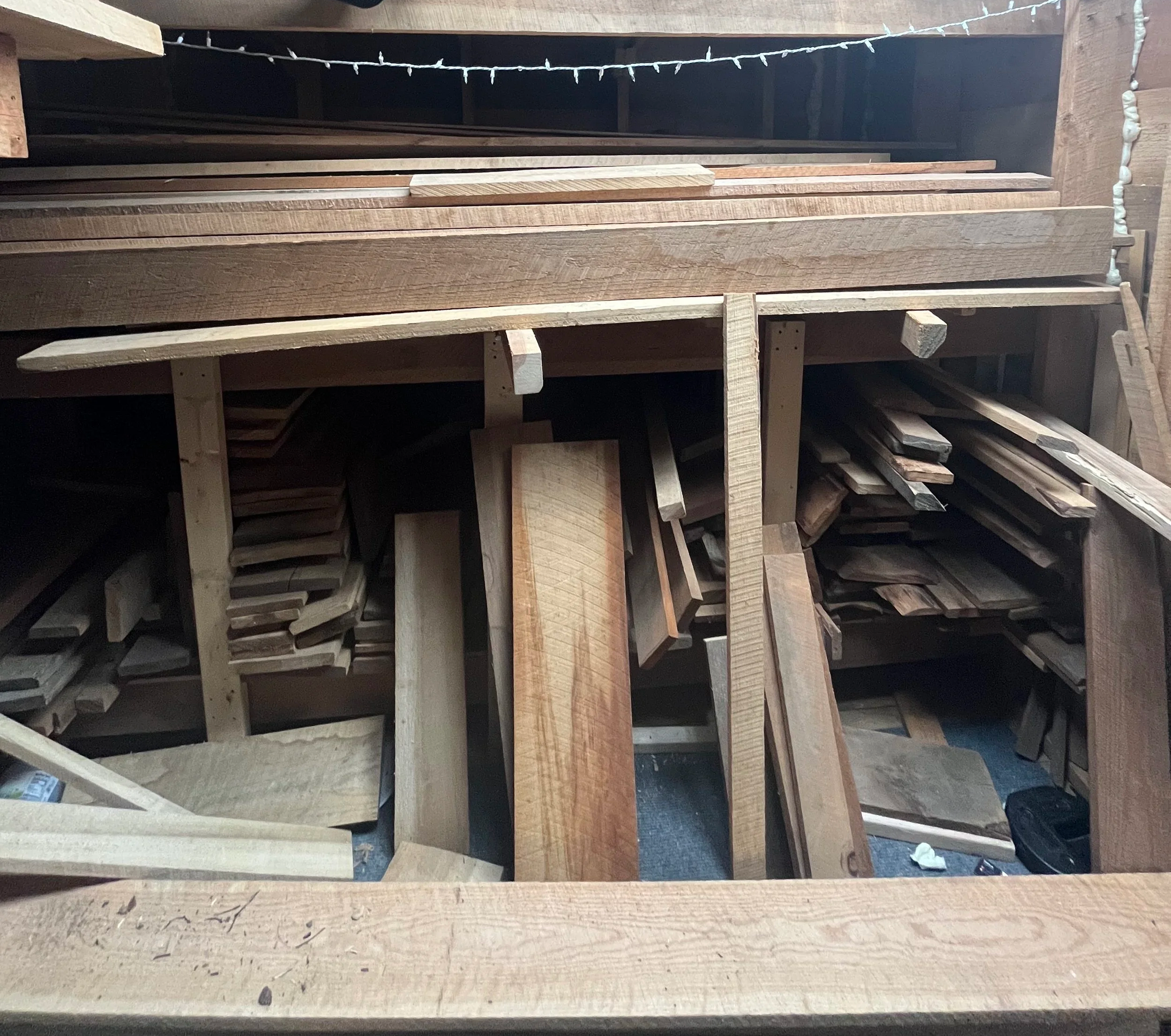 Stacks of various wooden planks and pieces stored in a woodworking shop or storage area.