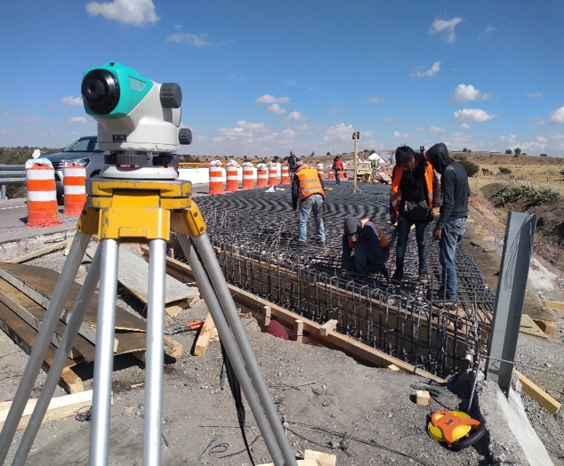 Trabajadores de la construcción en una obra de construcción de carreteras con un nivél óptico en primer plano.