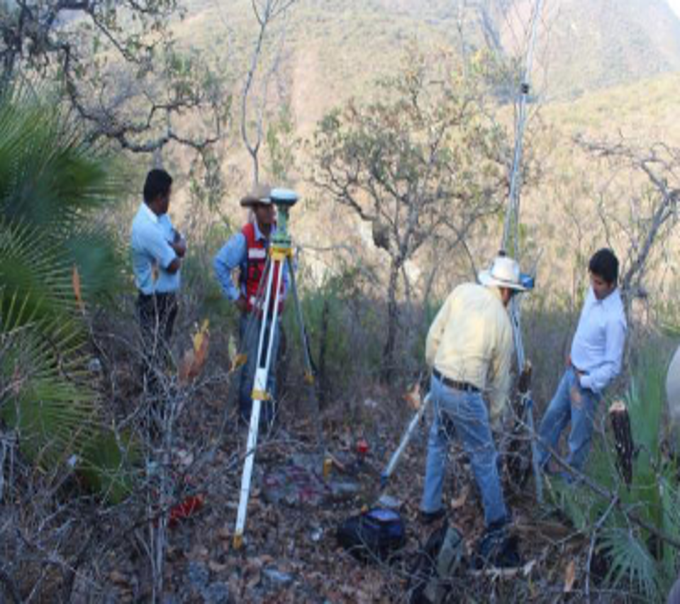 Personas realizando mediciones topográficas en un área de vegetación árida con árboles dispersos.