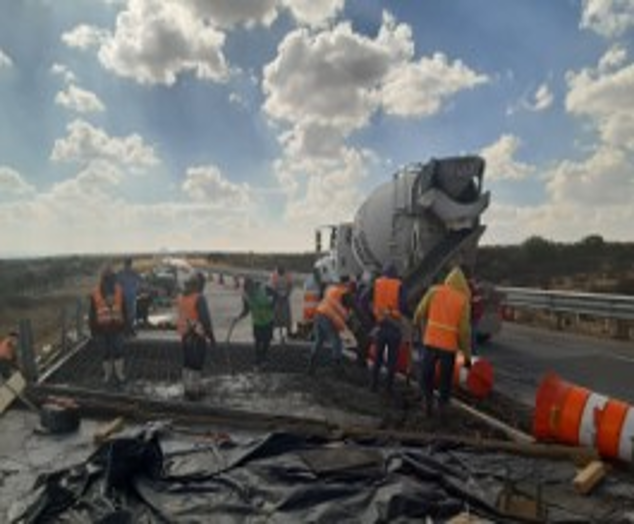 Camión volteado en una autopista con trabajadores y carros cercanos en un día soleado.
