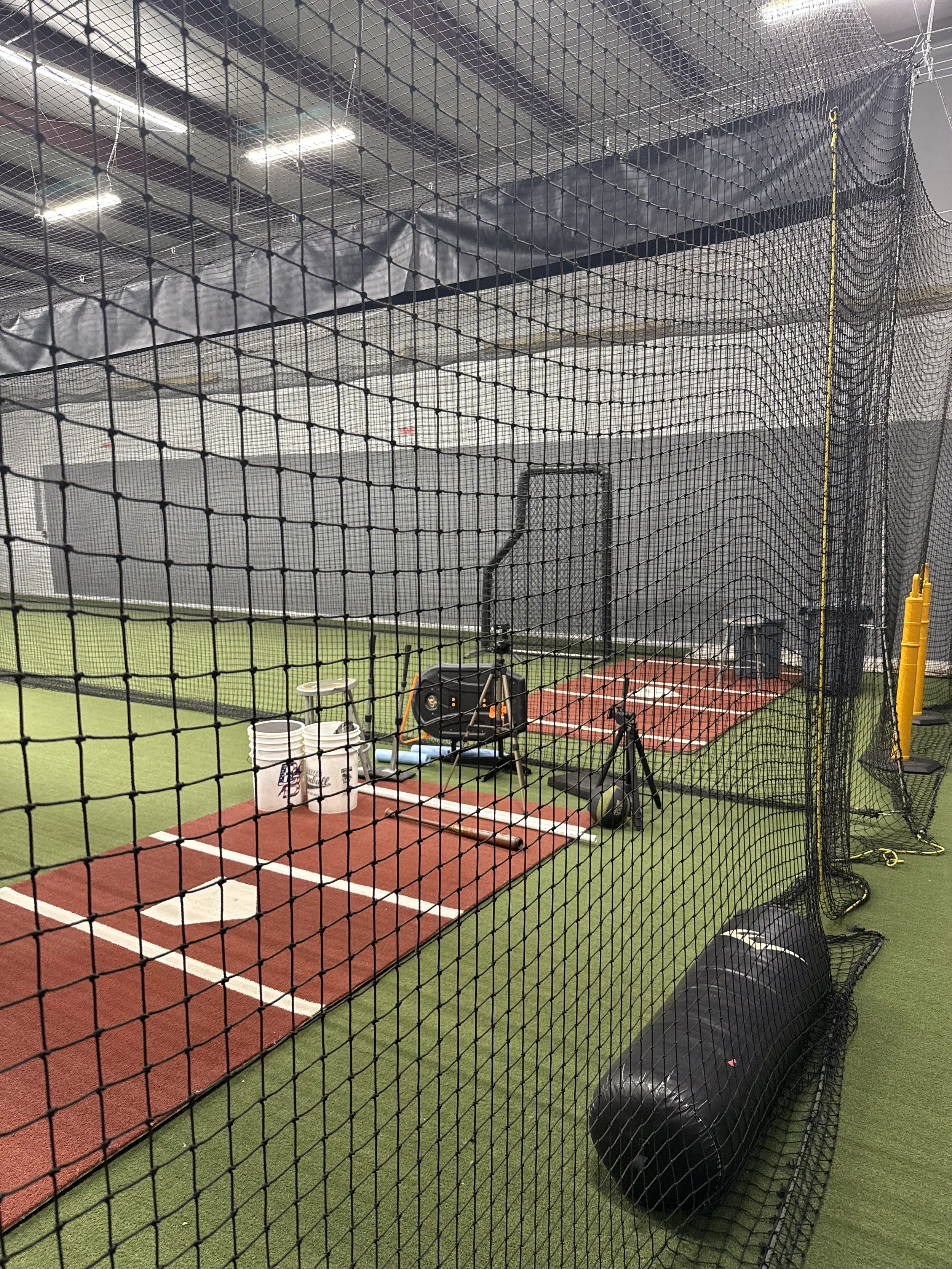 An indoor golf practice bay with artificial turf, a hitting mat, golf balls, a golf swing trainer, and nets surrounding the area for safety.