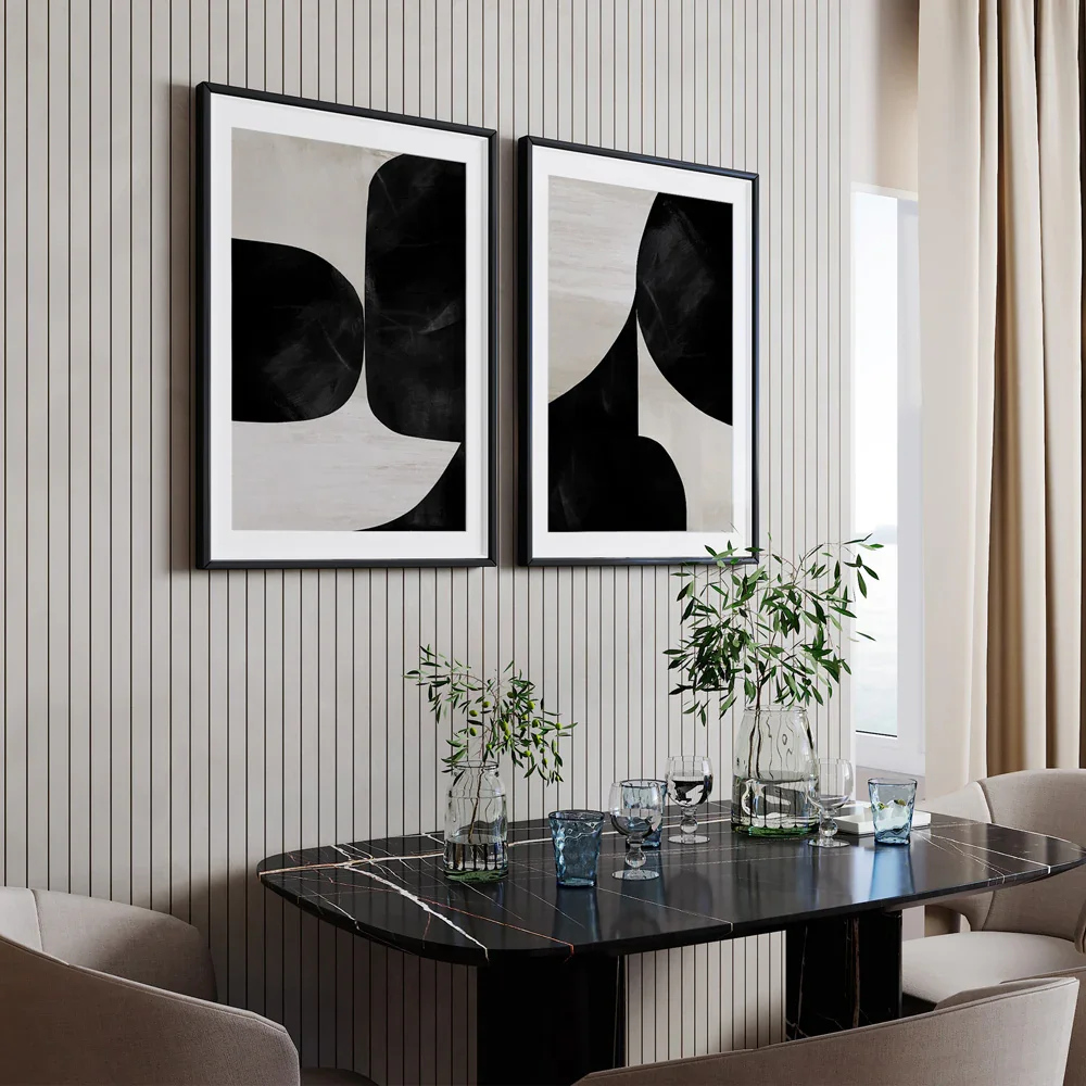 Interior dining room with a black marble table, beige chairs, two abstract black and white framed artworks, and a window with beige curtains. There are two glass vases with green leafy branches and several drinking glasses on the table.