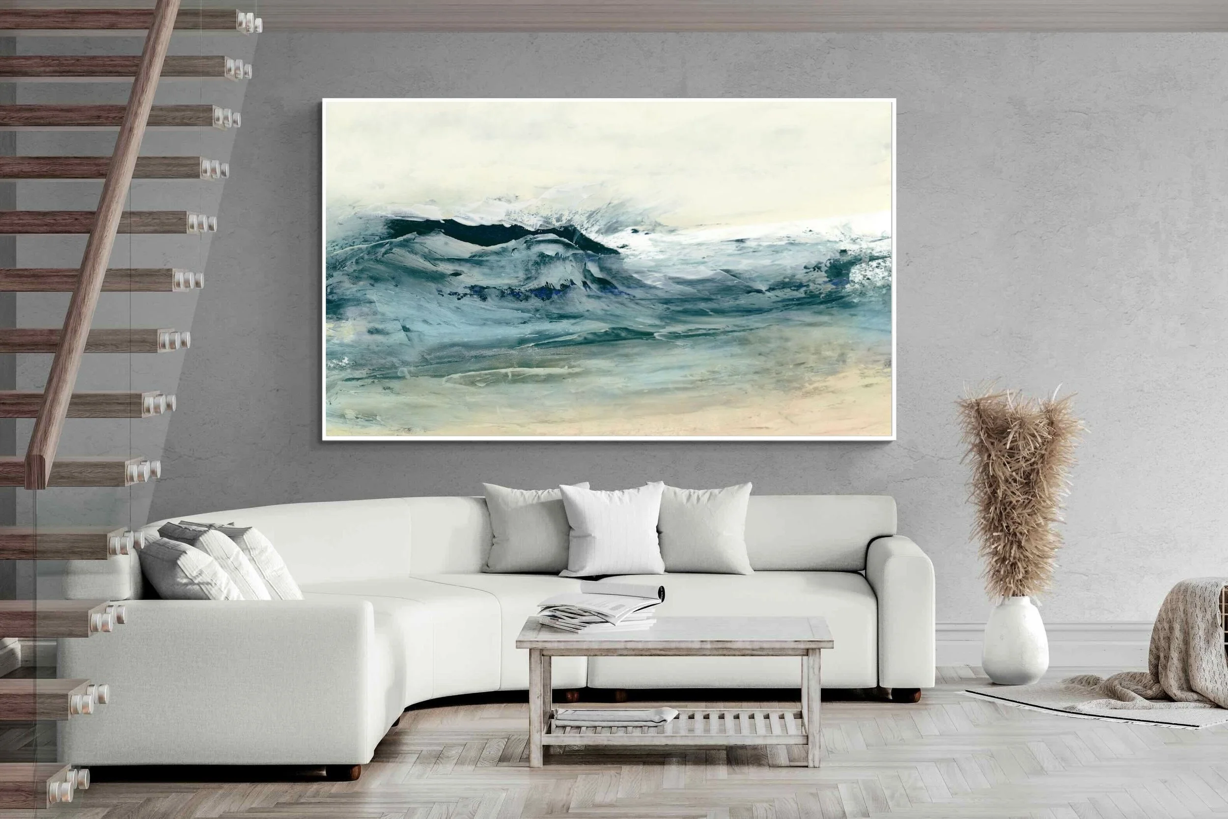 Modern living room with a white sectional sofa, a coffee table with books, a large abstract ocean painting on the wall, a tall decorative plant in a vase, and a staircase on the left side.
