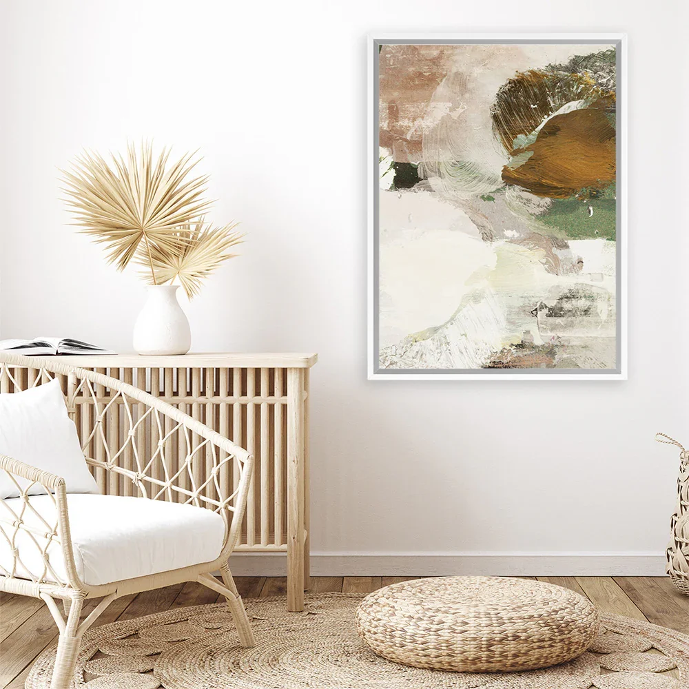 Interior with a rattan chair, a wooden console table with a white vase holding dried palm leaves, abstract artwork on the wall, a woven pouf on a circular rug.