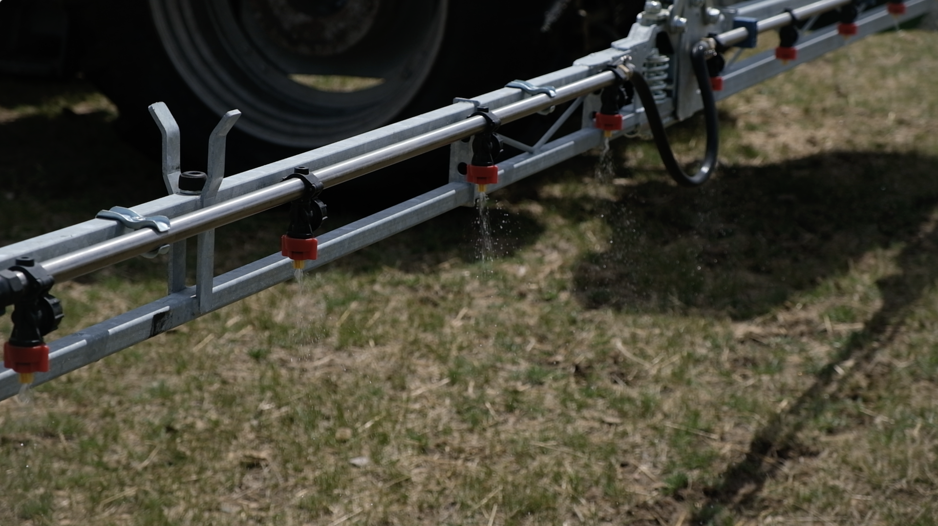 Metal irrigation system with water flowing from small red nozzles, set on dry grassy ground.