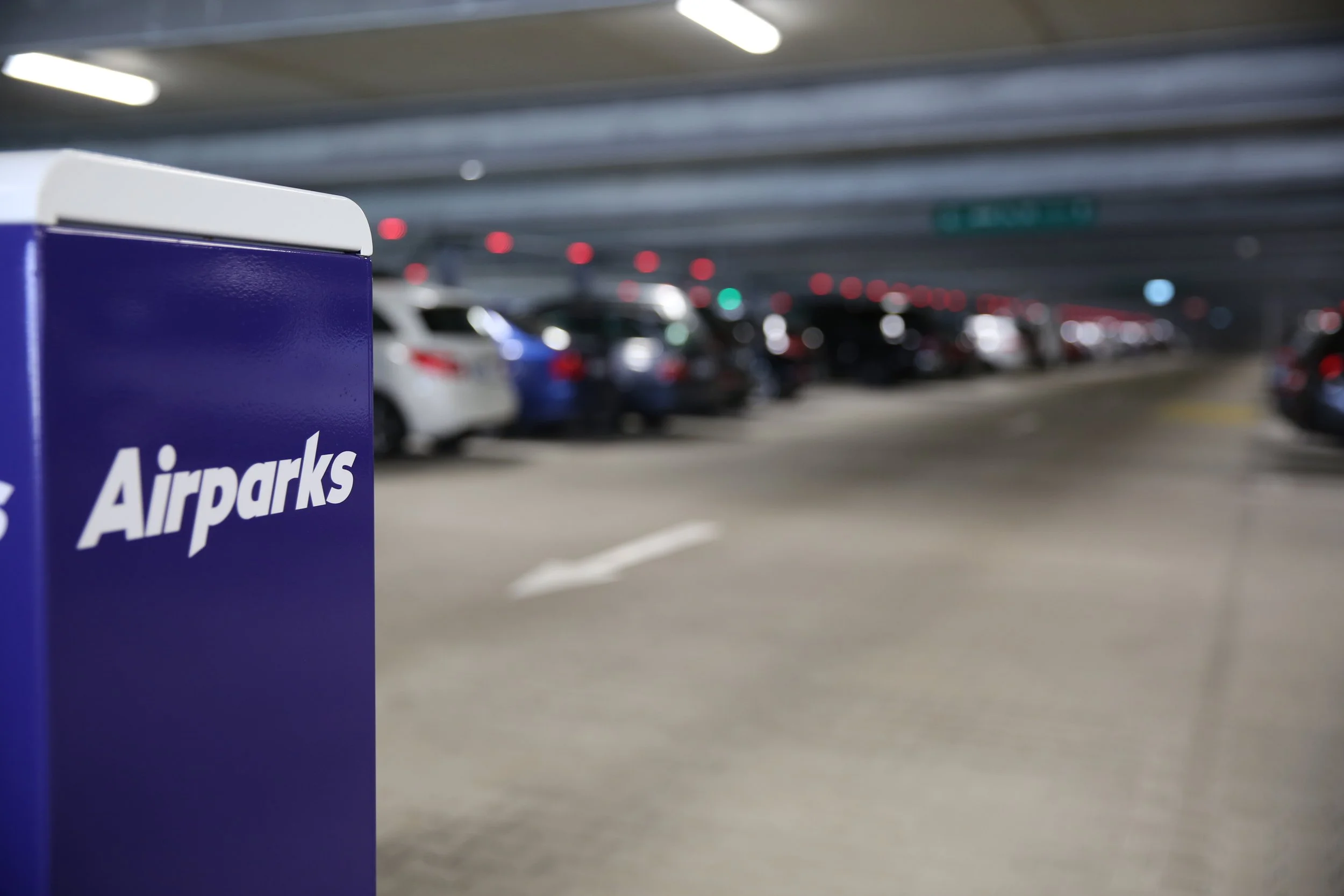 Blaue Parkbox mit der Aufschrift 'Airparks' in einem Parkhaus, im Hintergrund sind Autos und das Parkhausdach sichtbar.