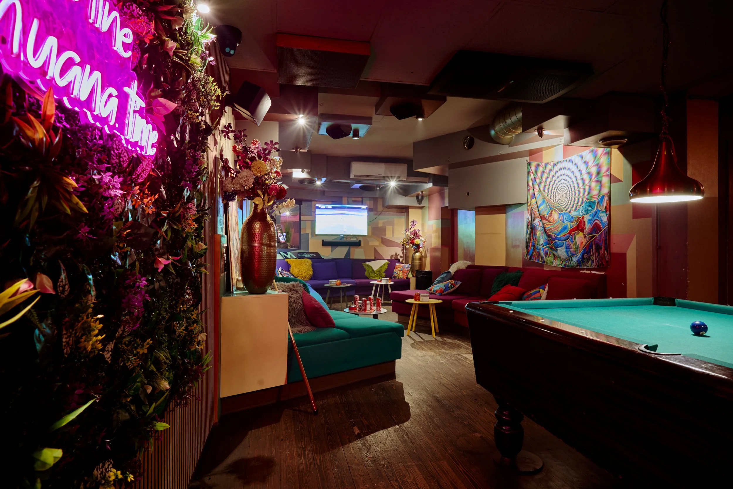 Gezellige indoor lounge met ligbedden, bloemen, een tv, een pooltafel en kleurrijke decoraties en verlichting.