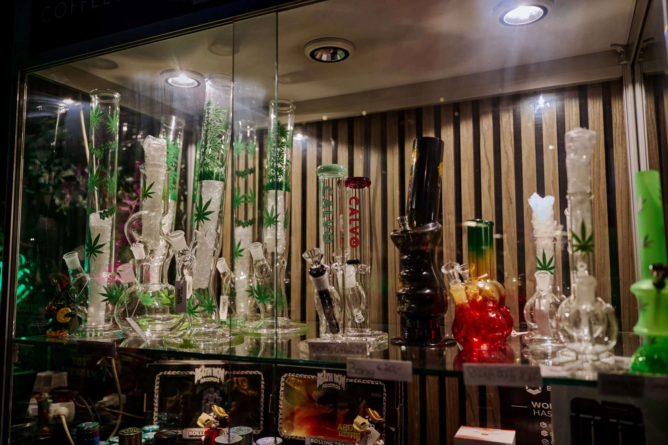 Glazen bollen met cannabisbladmotief en andere kleurrijke glassoorten in een winkeldisplay.