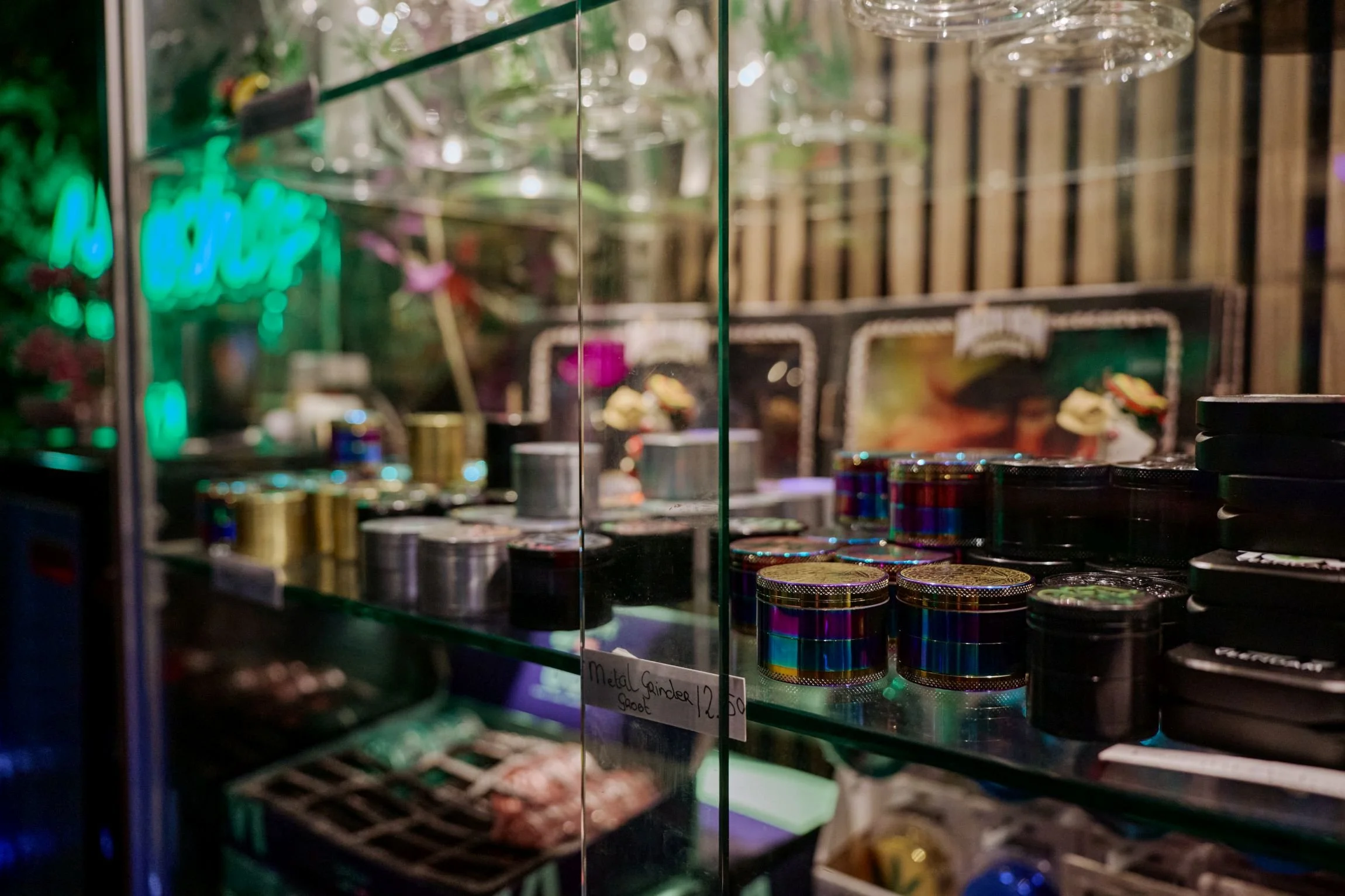 Glas met verschillende metalen en kleurrijke small containers op een glazen schap, met een houten wand en neonlicht op de achtergrond.