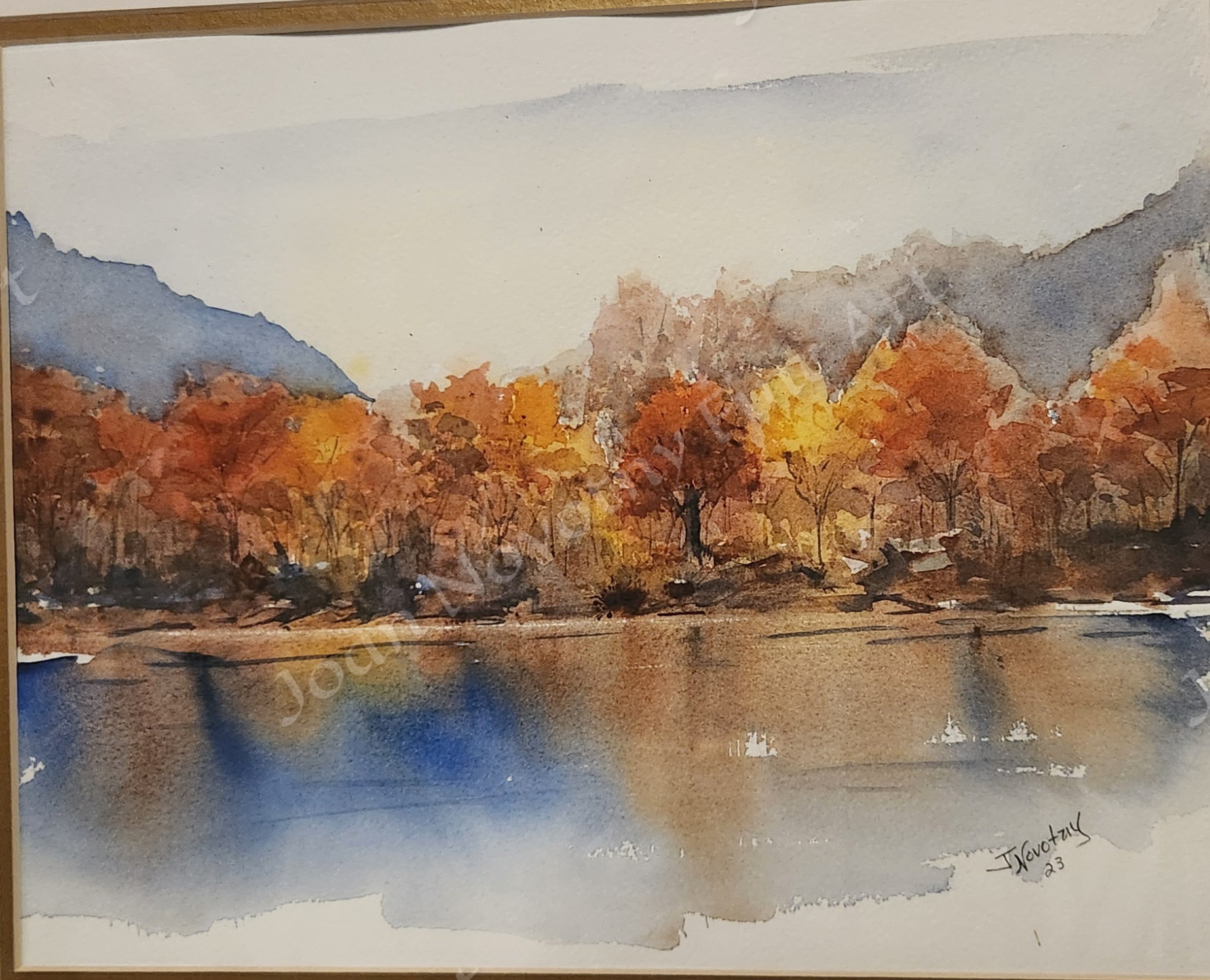Watercolor painting of a lakeside scene with orange, yellow, and brown trees, with mountains in the background and reflections in the water.