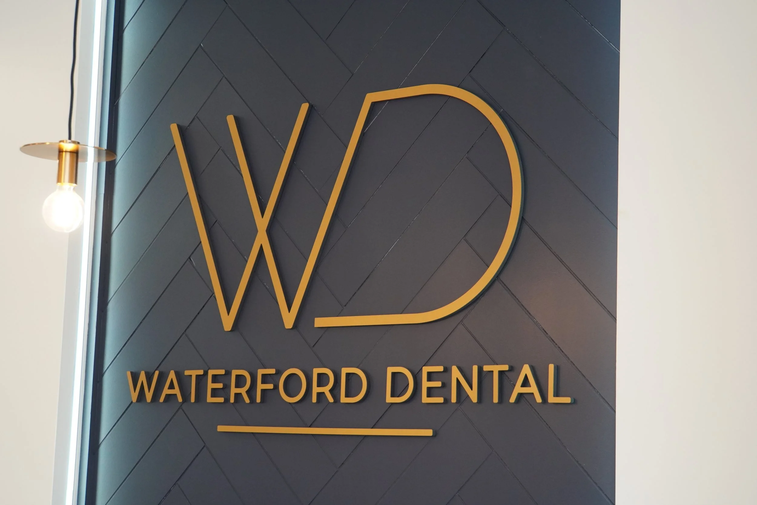 Yellow outlined letter W and the words Waterford Dental on a dark tiled wall