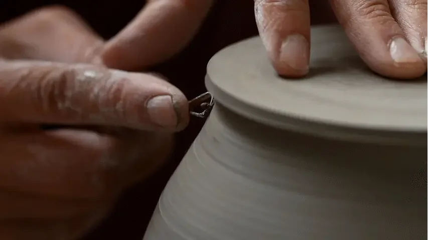 Close-up of hands shaping a ceramic vessel on a pottery wheel
