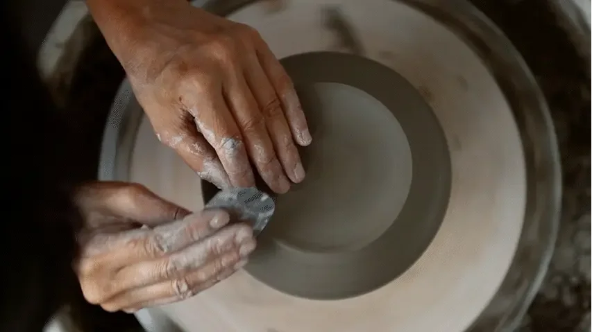 Hands shaping gray clay on a potter's wheel.