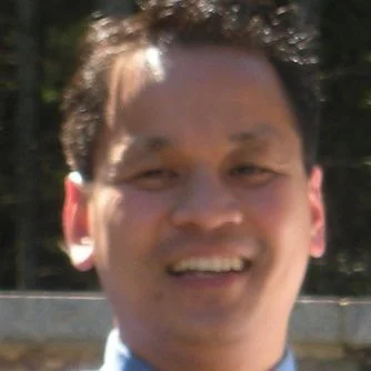 Close-up of a smiling man outdoors with trees in the background.
