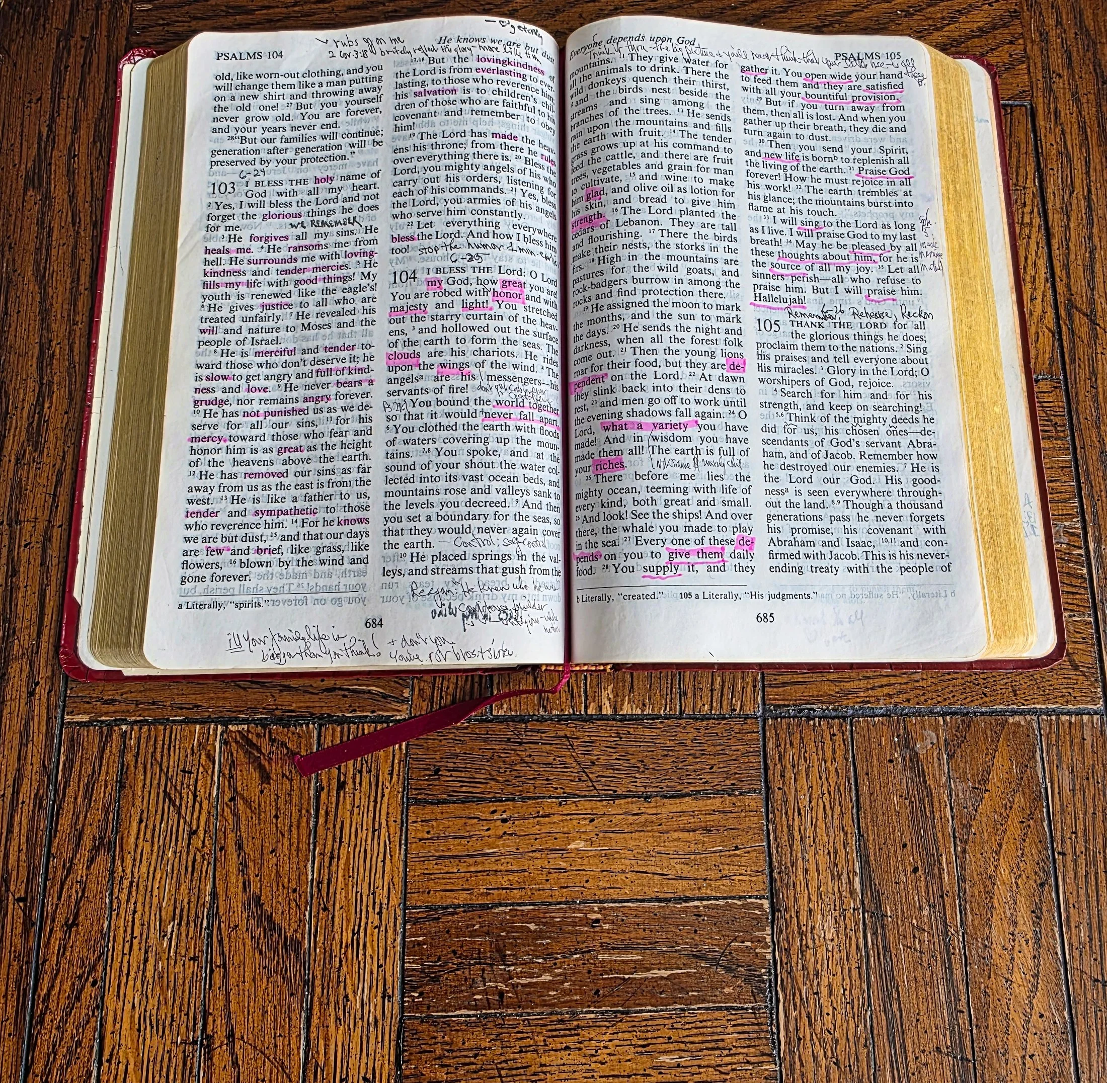 Open Bible showing highlighted scripture verses with handwritten notes in the margins. The Bible is on a wooden surface.