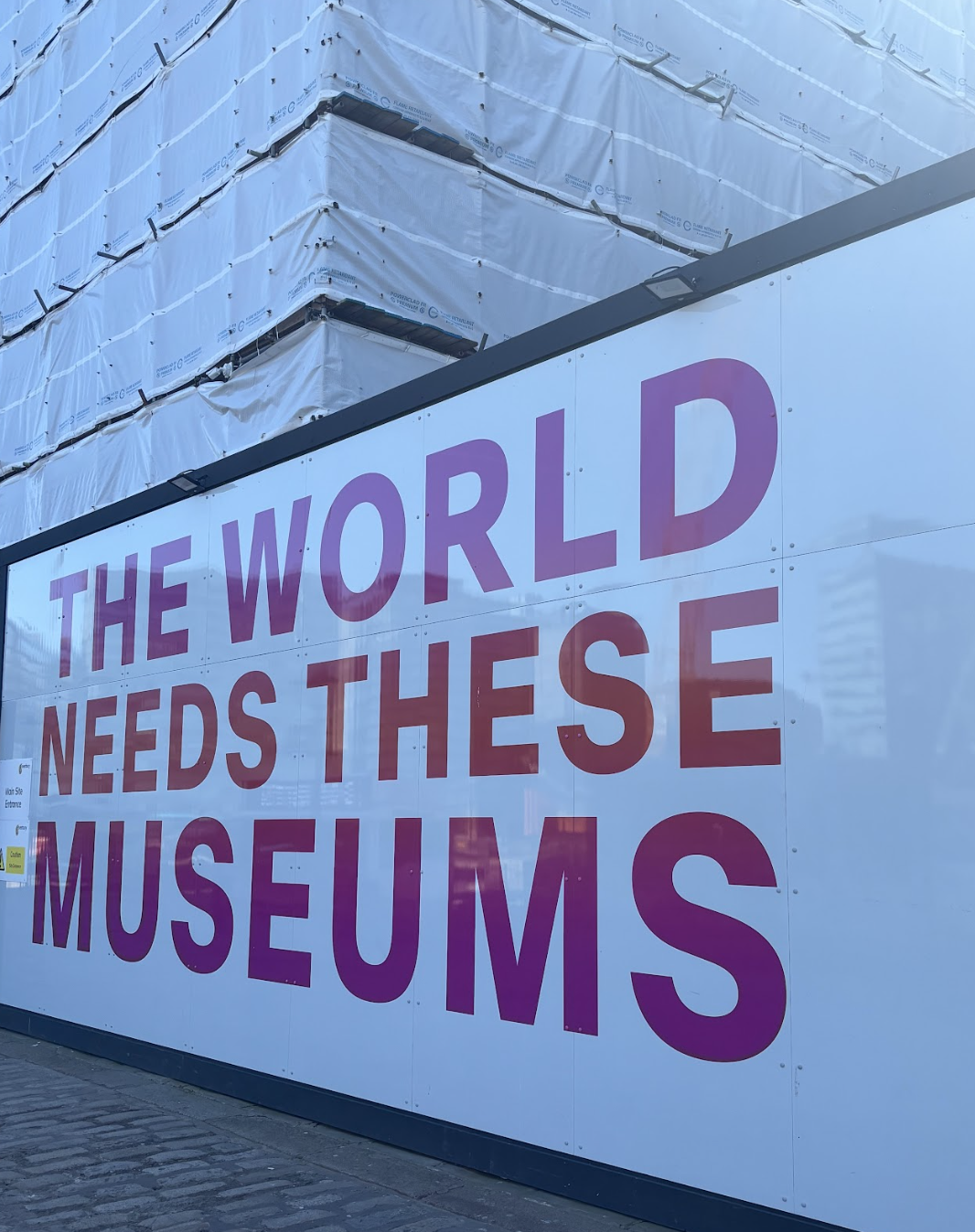 A large billboard with the message, "The world needs these museums," displayed in bold text.
