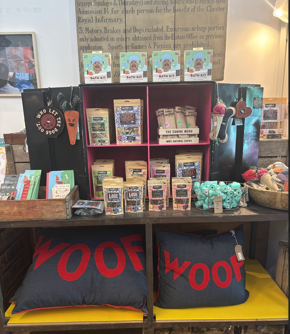Display of dog-related products including bath kits, treats, chew toys, and pillows with 'WOOF' printed on them.