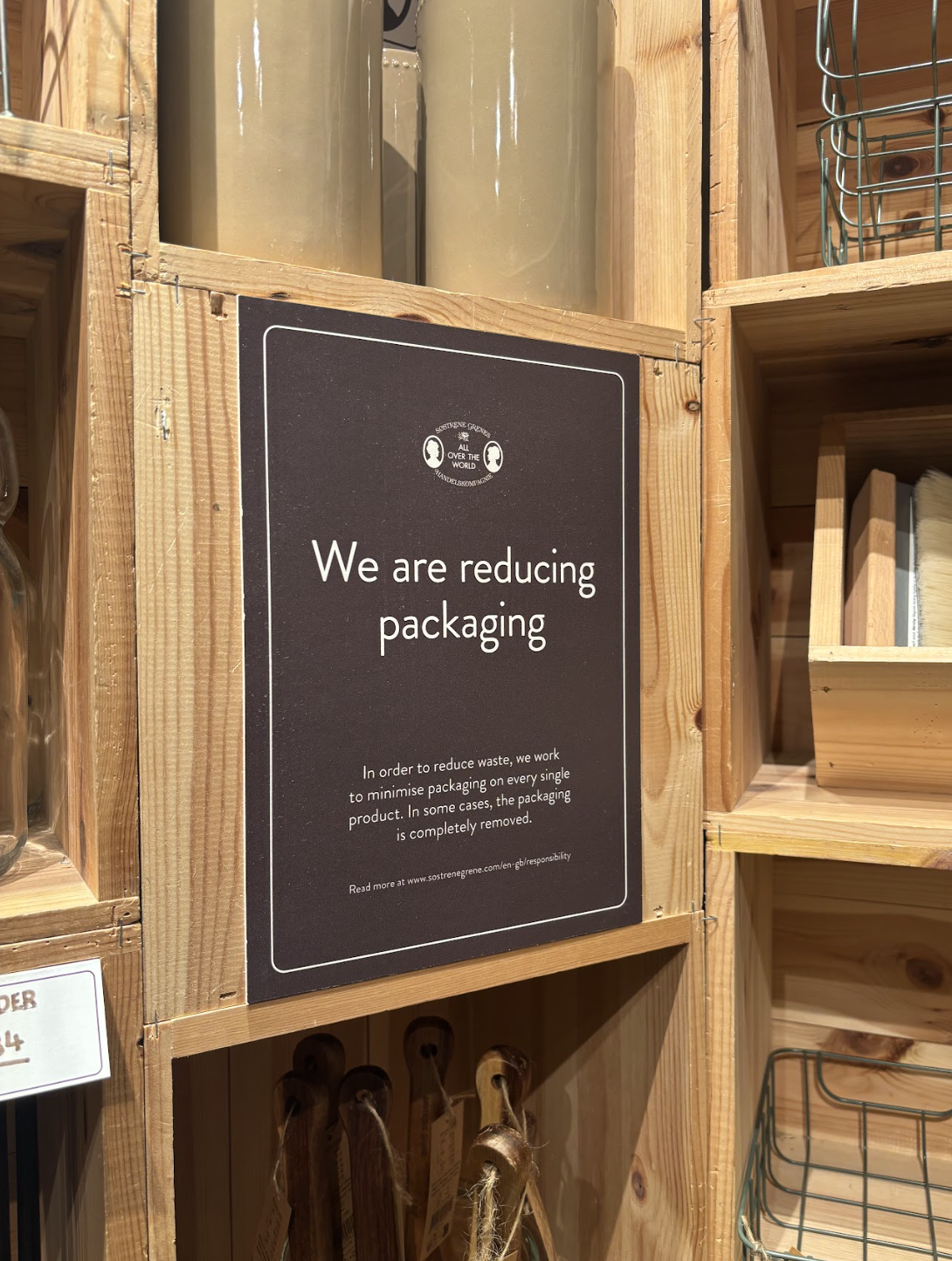 Sign on wooden shelf indicating efforts to reduce packaging waste in a store.