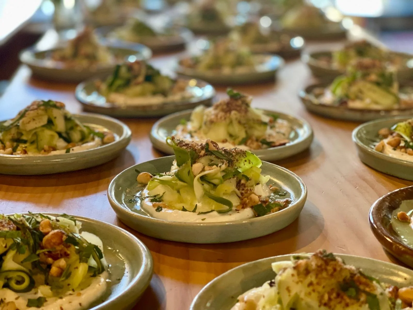 Several small plates of salad with greens, nuts, and cheese on a wooden table.