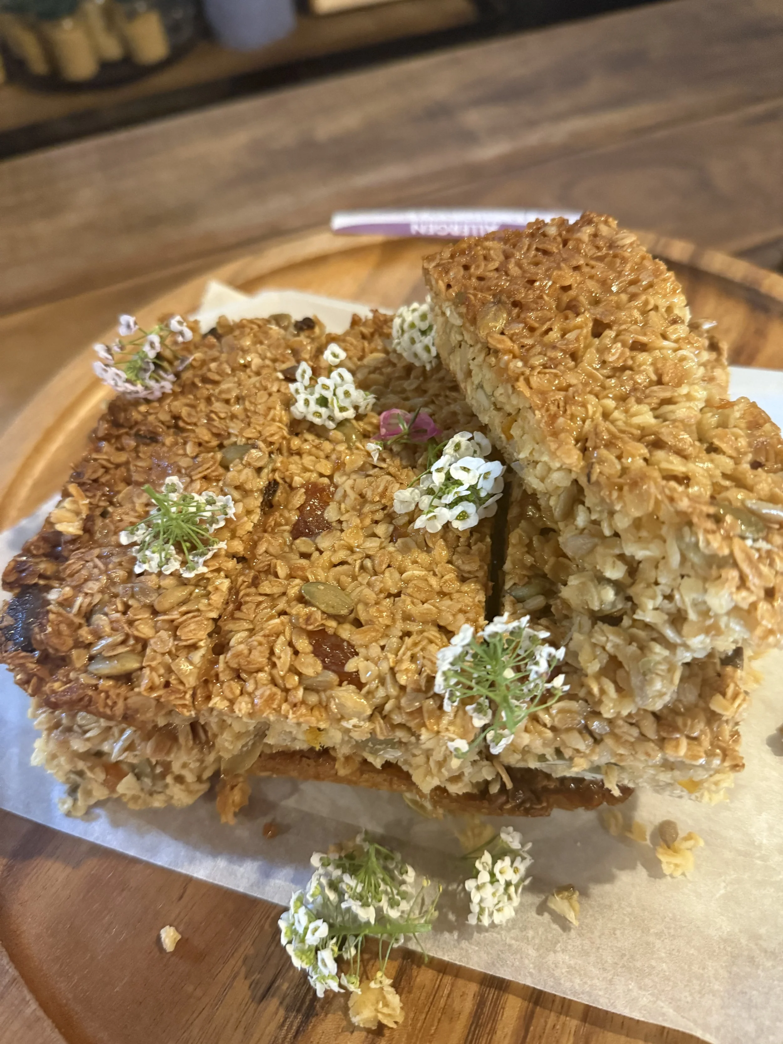 Close-up view of granola bars with oats and nuts, decorated with small white flowers on a wooden surface.