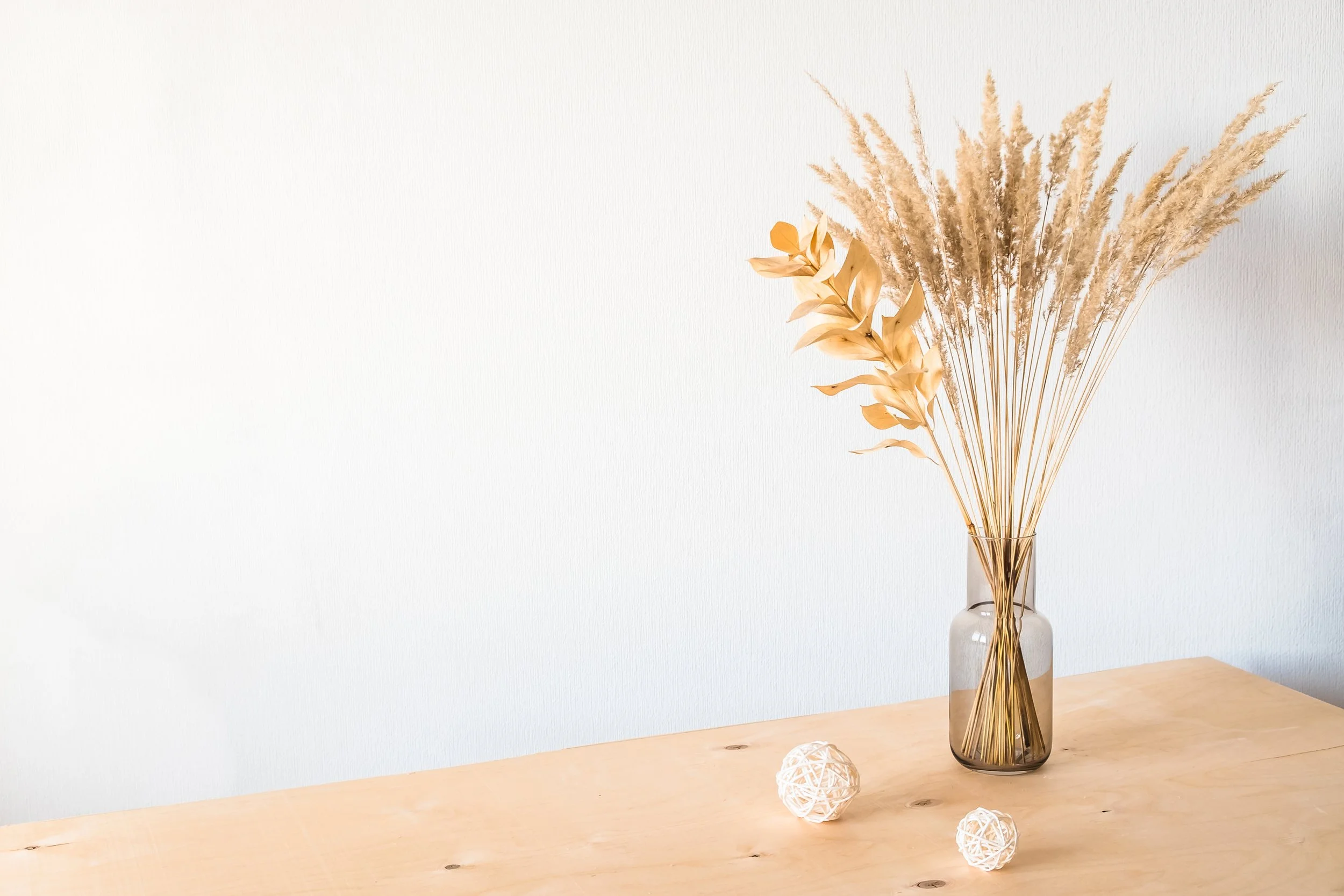 Dried botanical stems in a glass vase on a wooden table.