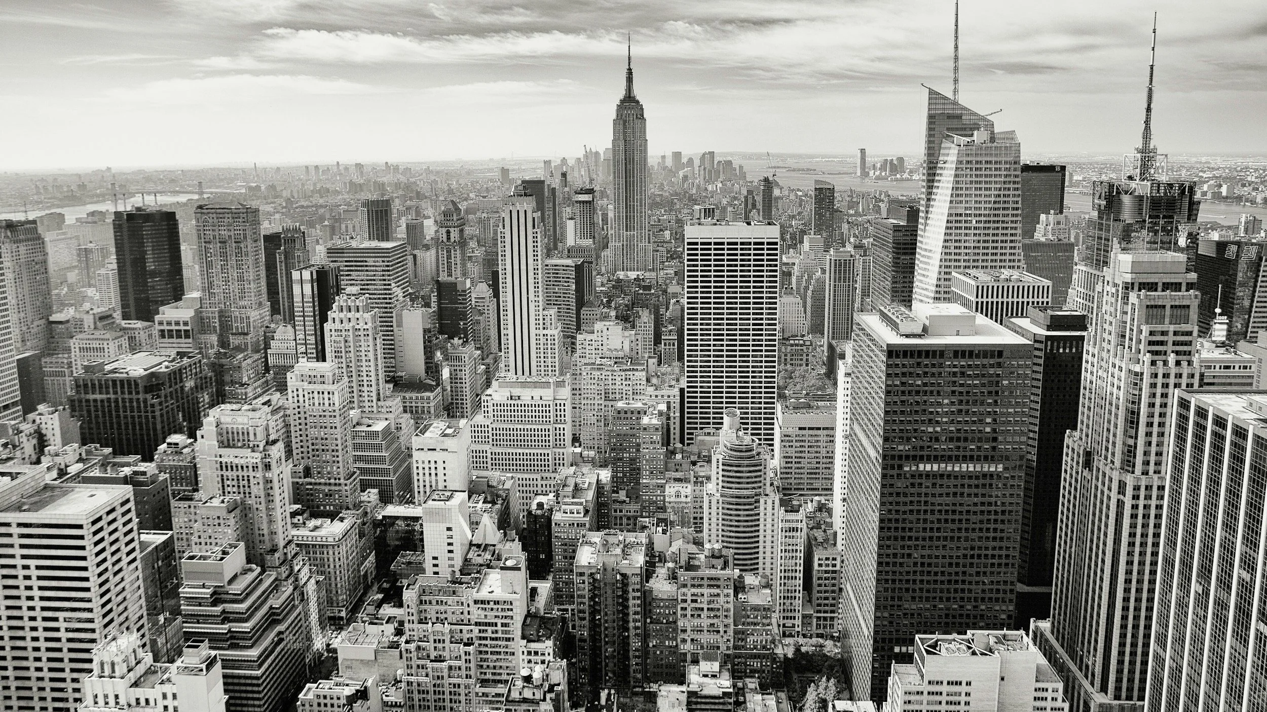 Black and white aerial view of New York City skyline with numerous skyscrapers, including the Empire State Building prominently in the center.