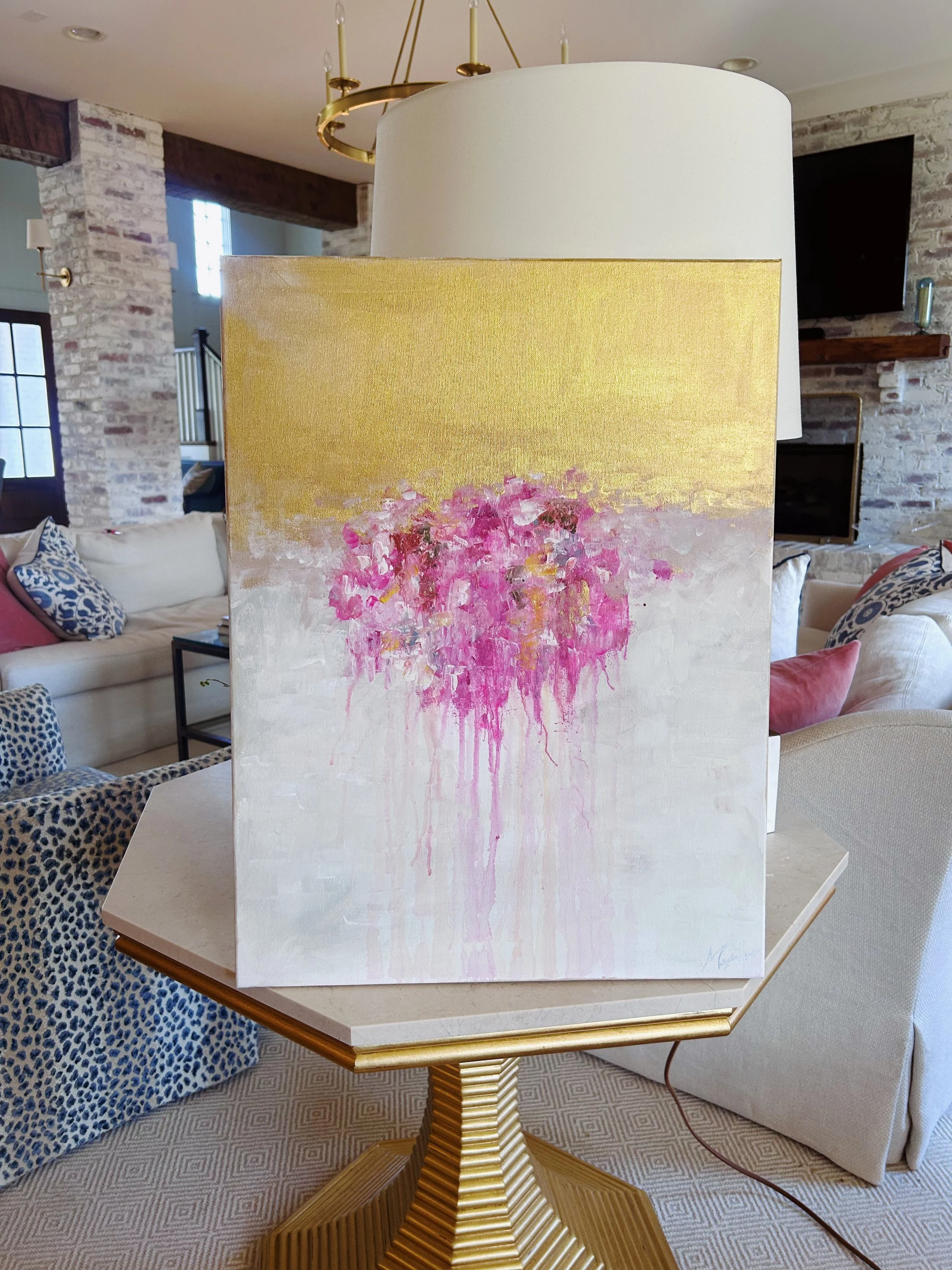 A painting of pink flowers with yellow and white background, placed on a small table in a living room.