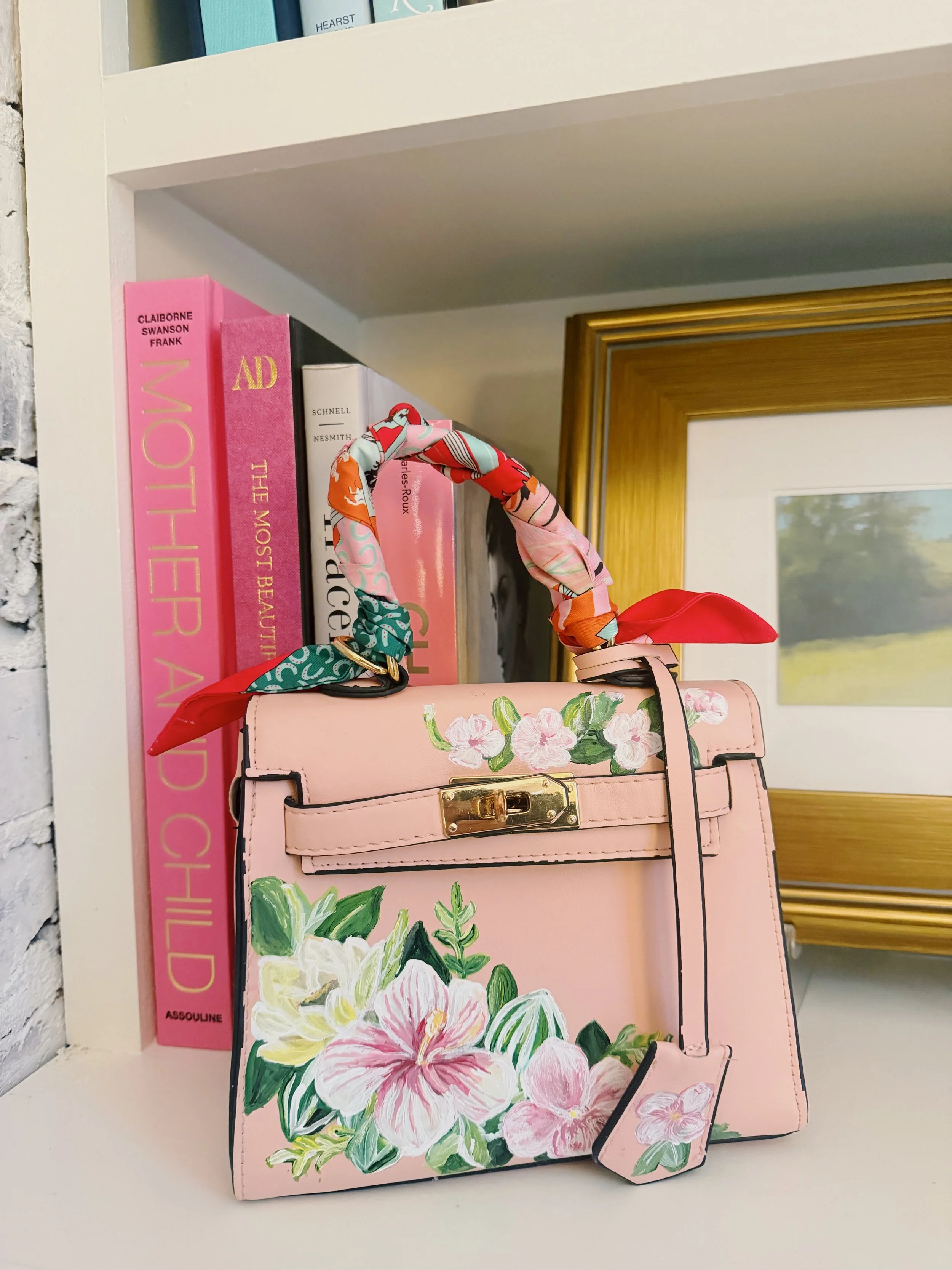 Pink handbag with floral design placed on a shelf with books in the background.