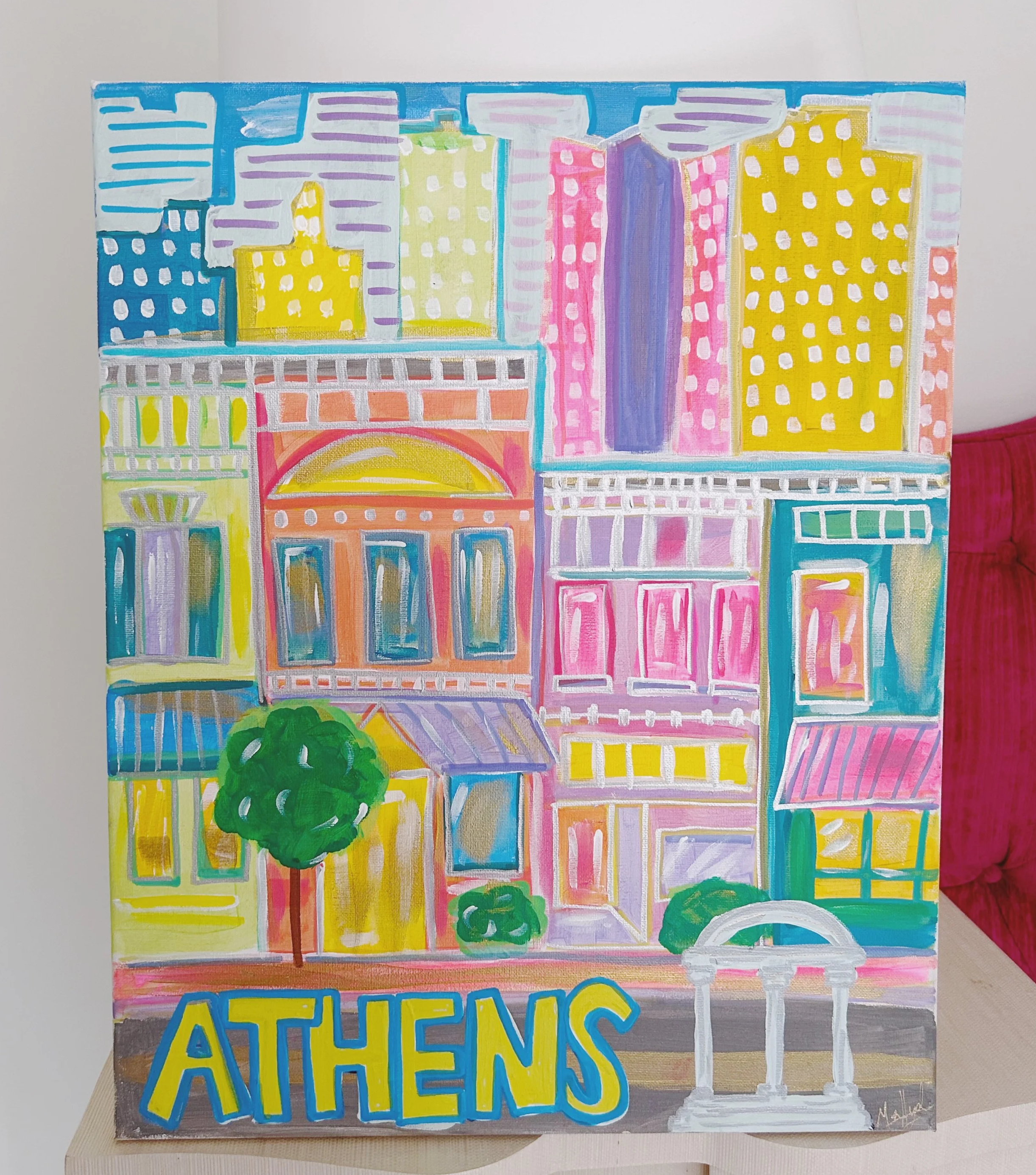 Colorful painting of buildings in Athens, with the word 'ATHENS' in large blue and yellow letters at the bottom. The artwork features various windows, awnings, trees, and architectural details in bright colors.