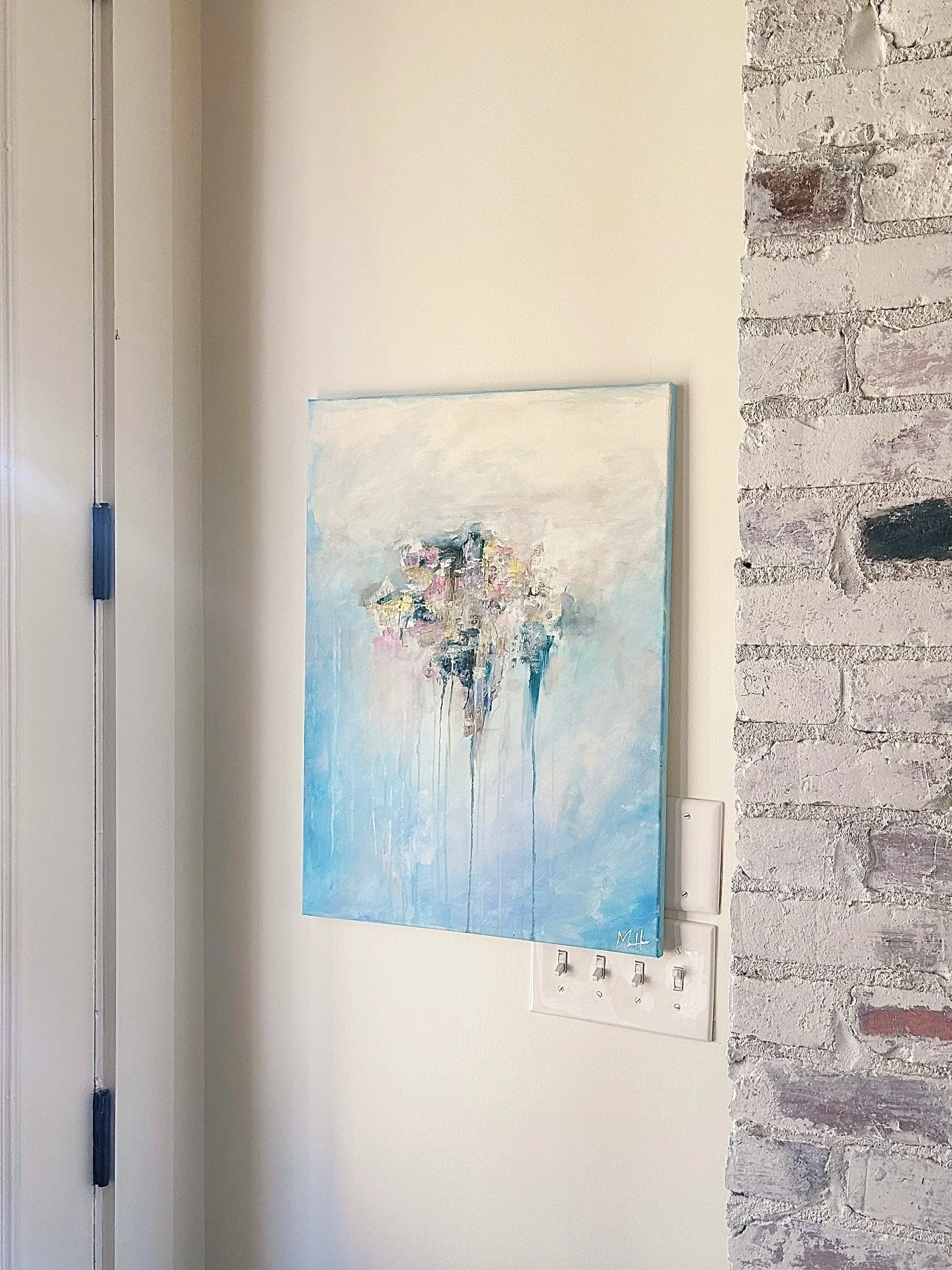 Interior corner of a room with a white wall, a brick accent wall, a colorful abstract painting, and light switches.
