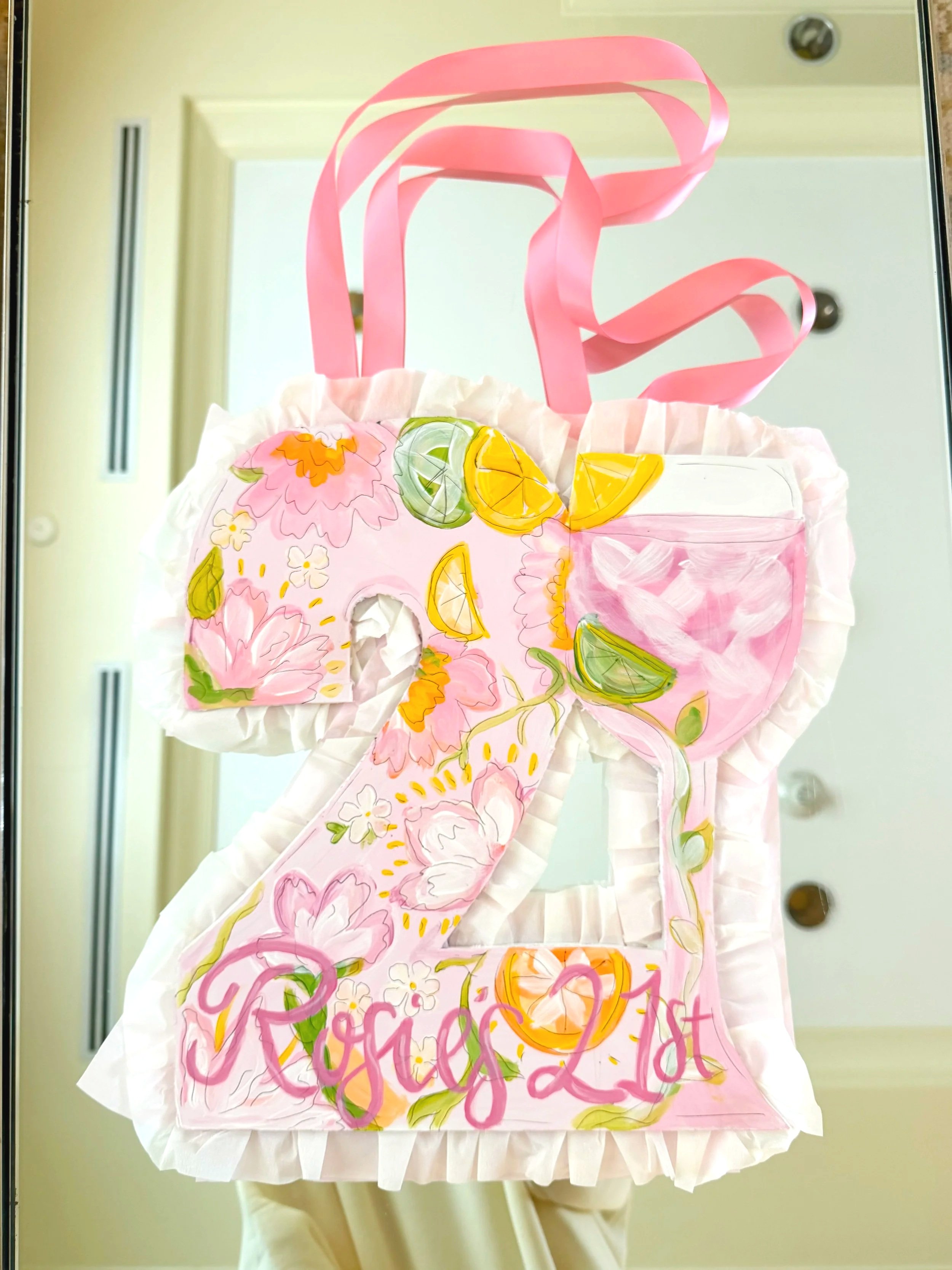 Decorated paper bag with pink floral and summer fruit designs, including lemons and limes, featuring the word 'Congratulations' written in pink at the bottom. The bag has pink ribbon handles and is placed on a mirror surface.