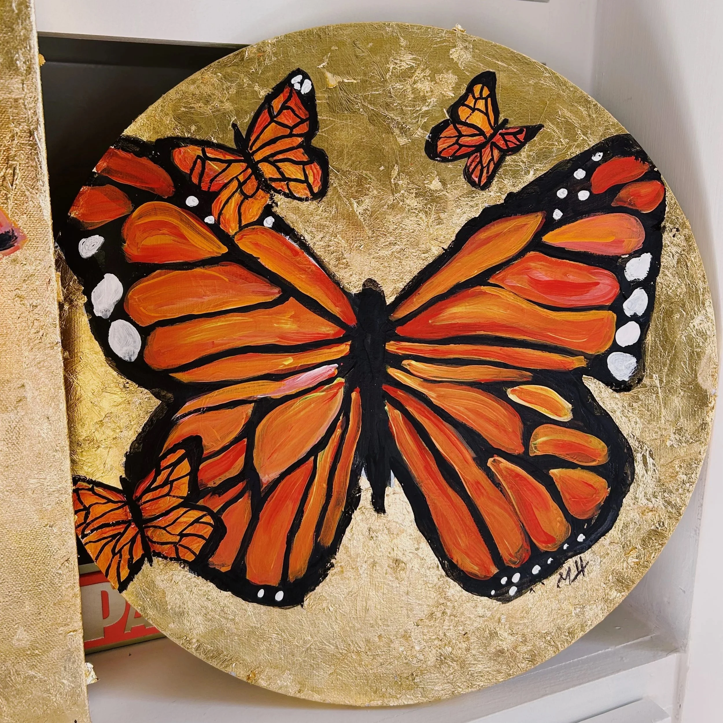Painting of a large monarch butterfly with orange and black wings, surrounded by two smaller butterflies on a gold background.